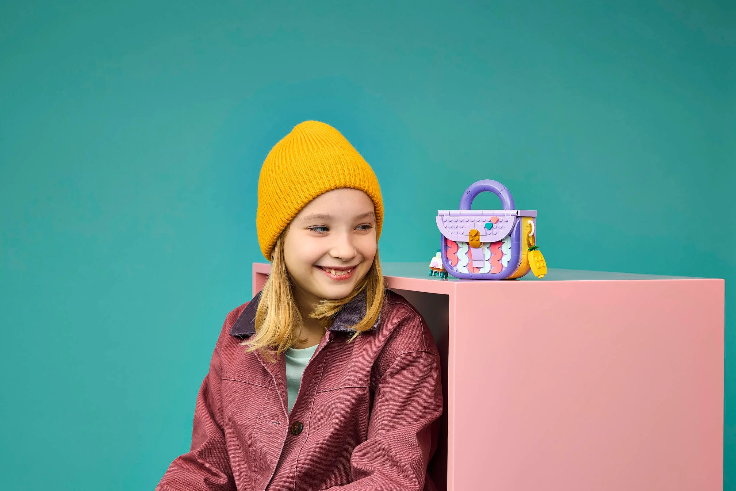 O fată zâmbitoare stă lângă o geantă LEGO Creator, promovând setul 31391.