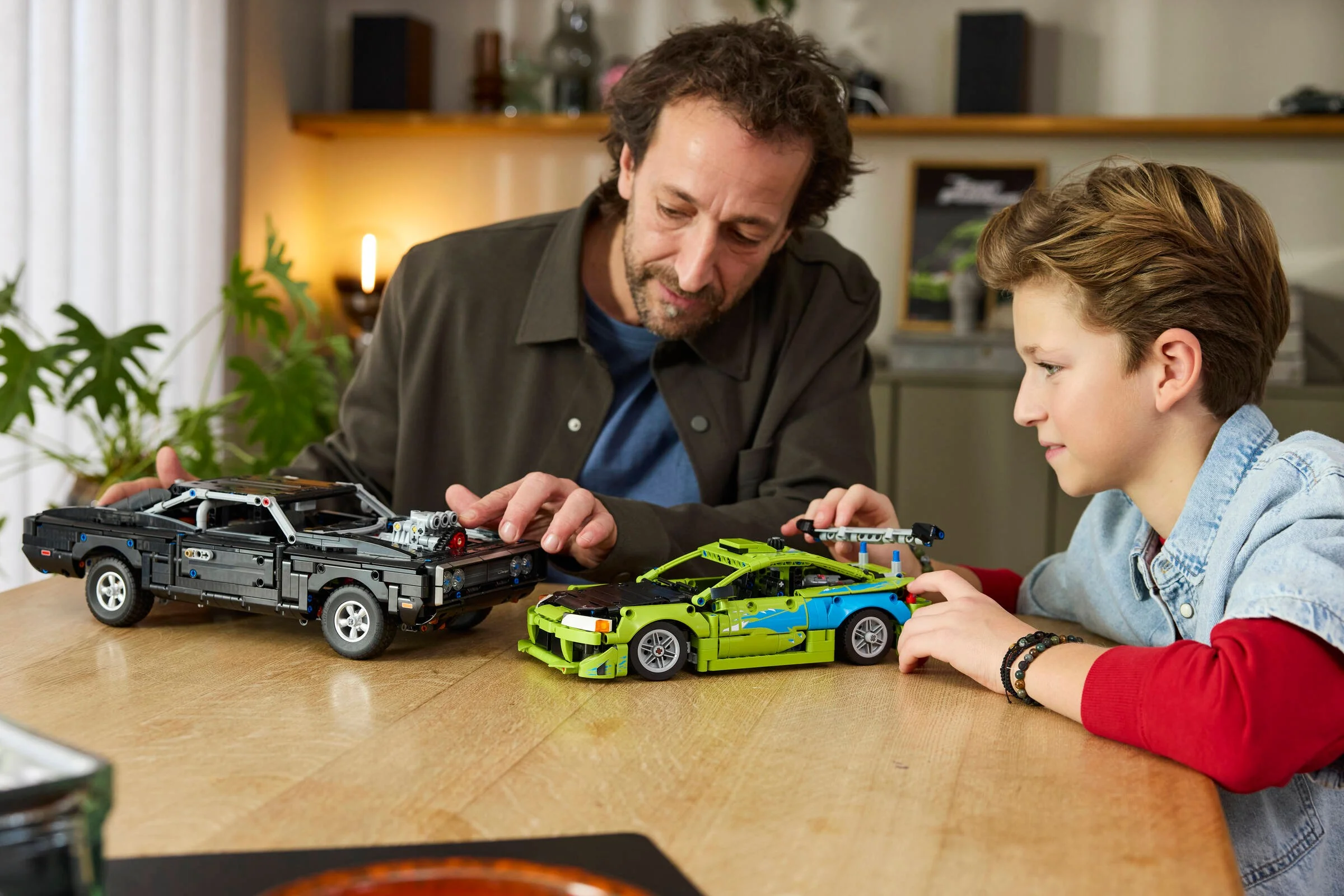Tată și fiu admiră modelele LEGO Technic Mitsubishi Eclipse și Dodge Charger.
