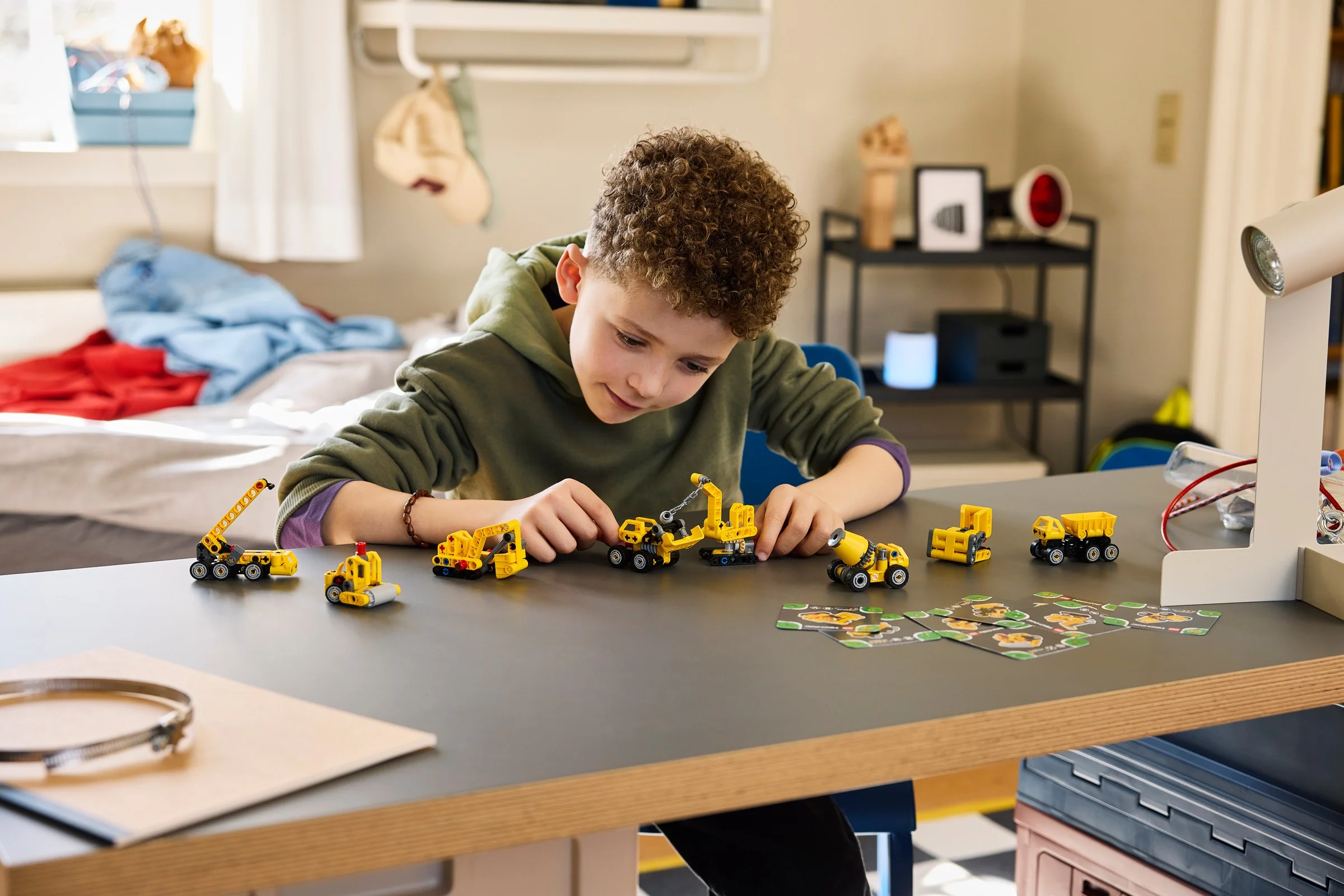 Băiatul se joacă cu diverse modele LEGO mici galbene, probabil din setul de construcție.