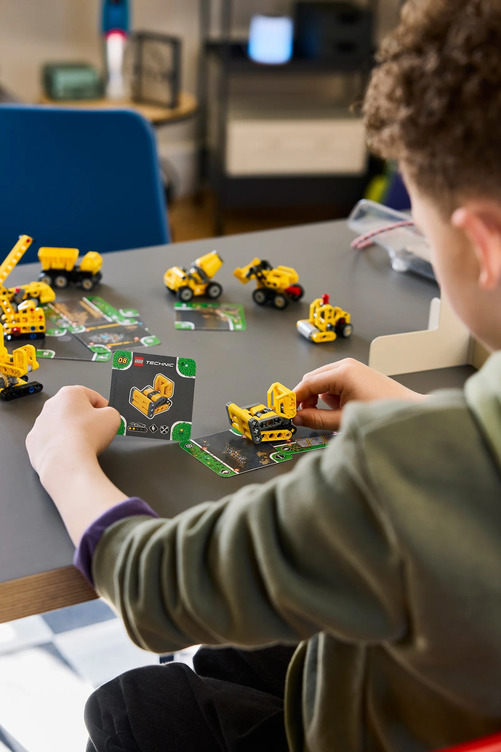 Copil construind modele LEGO Technic mici, urmând instrucțiunile de pe cartonașe.