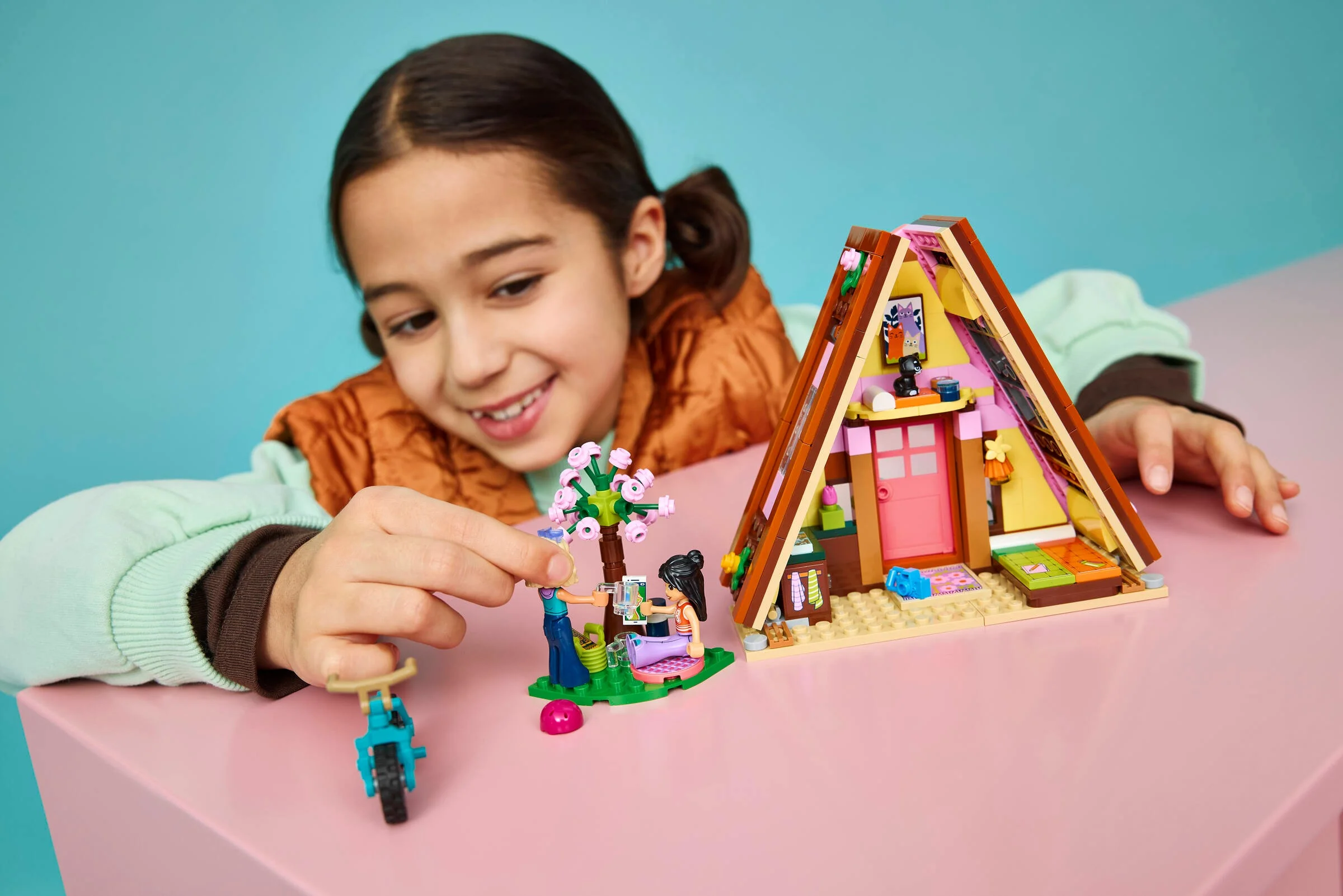O fată zâmbitoare se joacă cu cabana LEGO Friends, explorând aventurile din natură.