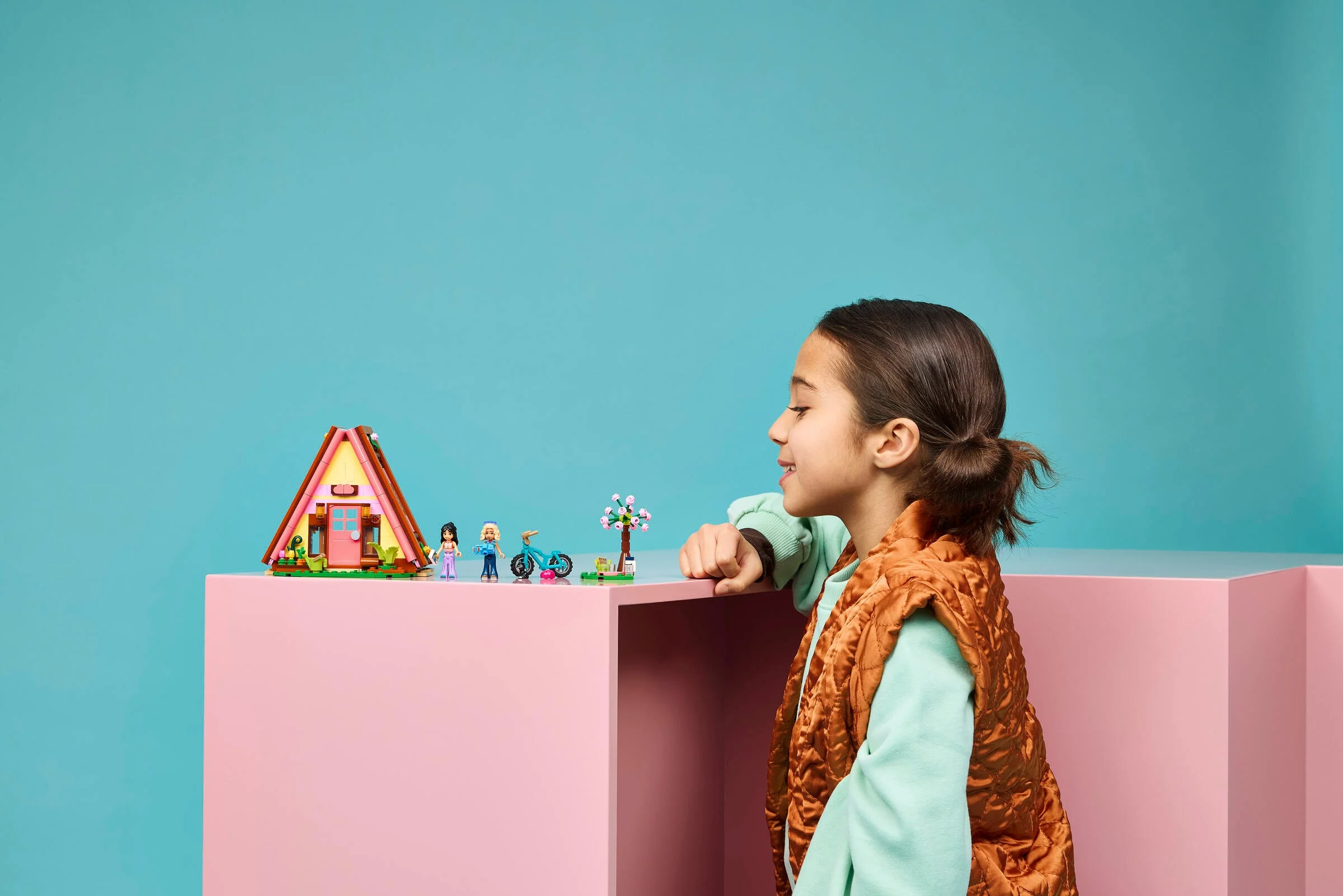 O fetiță zâmbește privind cabana LEGO de glamping. Imagine prietenoasă și plină de bucurie.