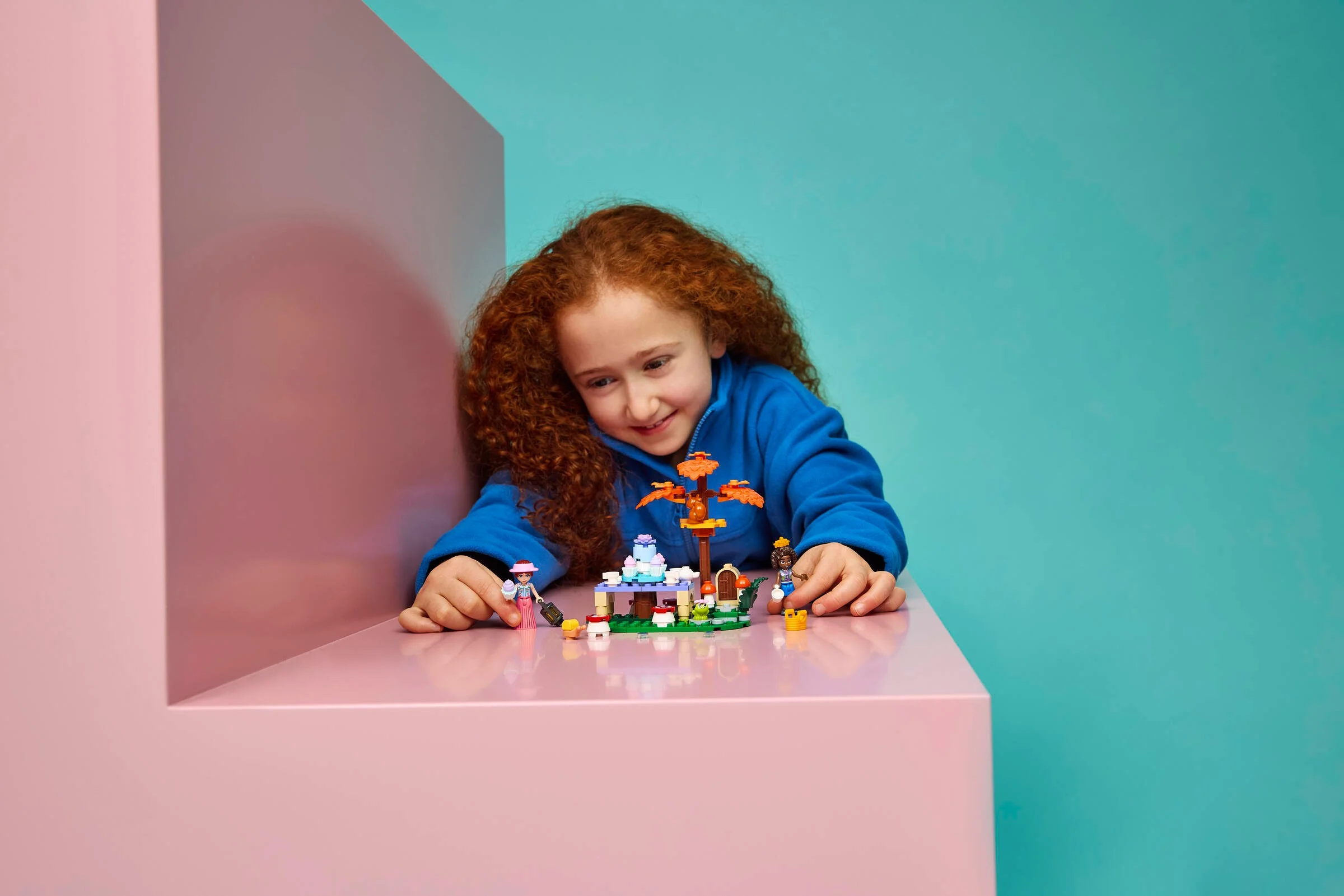 O fetiță se joacă cu setul LEGO Forest Tea Party, zâmbind încântată.