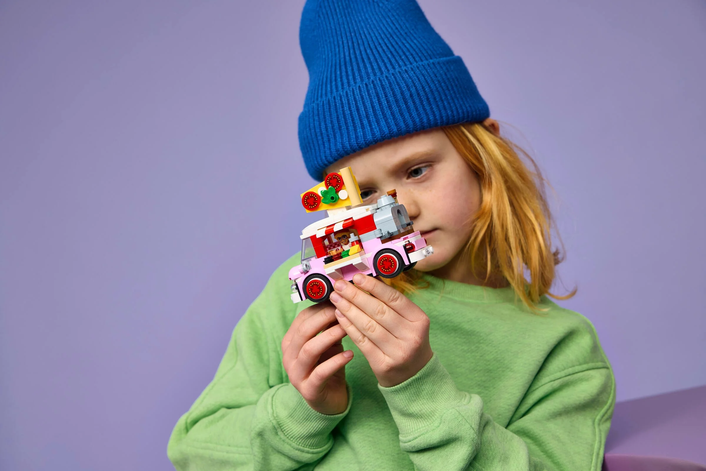 Fată ținând în mâini camionul de pizza LEGO Friends 42694, zâmbind. Distracție culinară garantată!