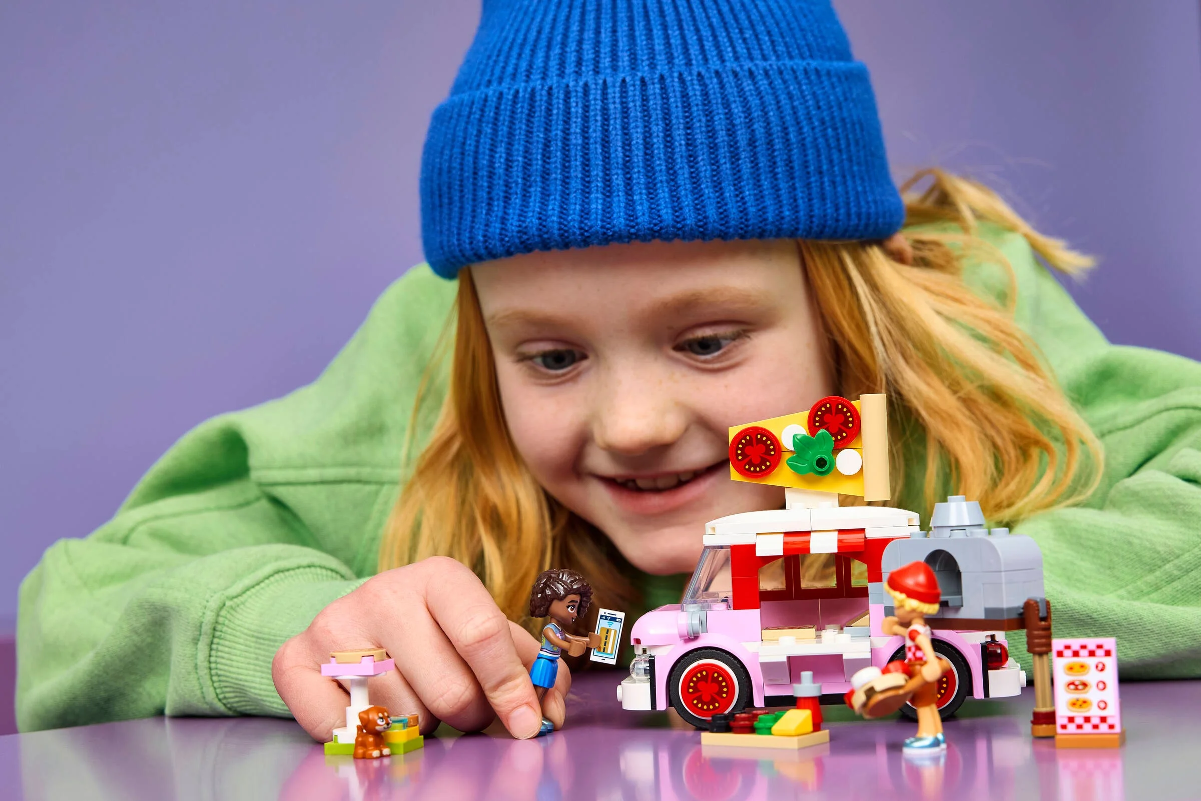 Fetiță se joacă cu camionul de pizza LEGO Friends, explorând detaliile și figurinele colorate.