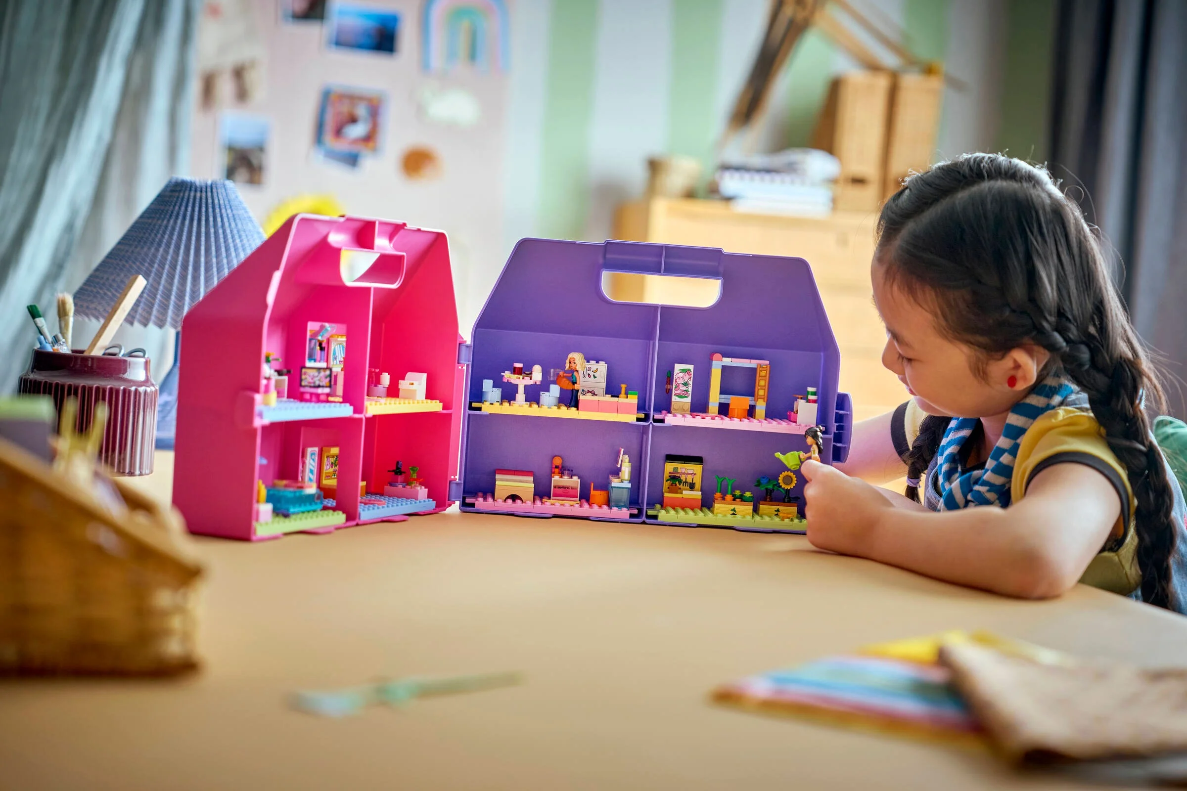 Fetiță se joacă cu setul LEGO Friends 42697, o căsuță de păpuși portabilă, roz și mov.