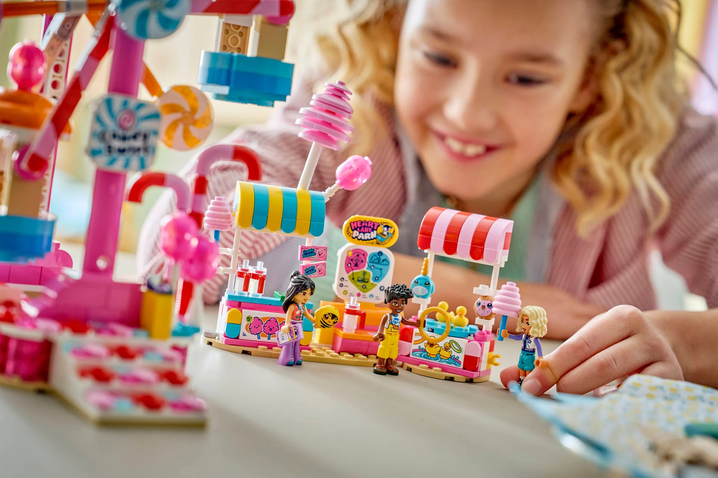O fată zâmbitoare se joacă cu setul LEGO Friends 42700, Roata Candy & Cupcake.
