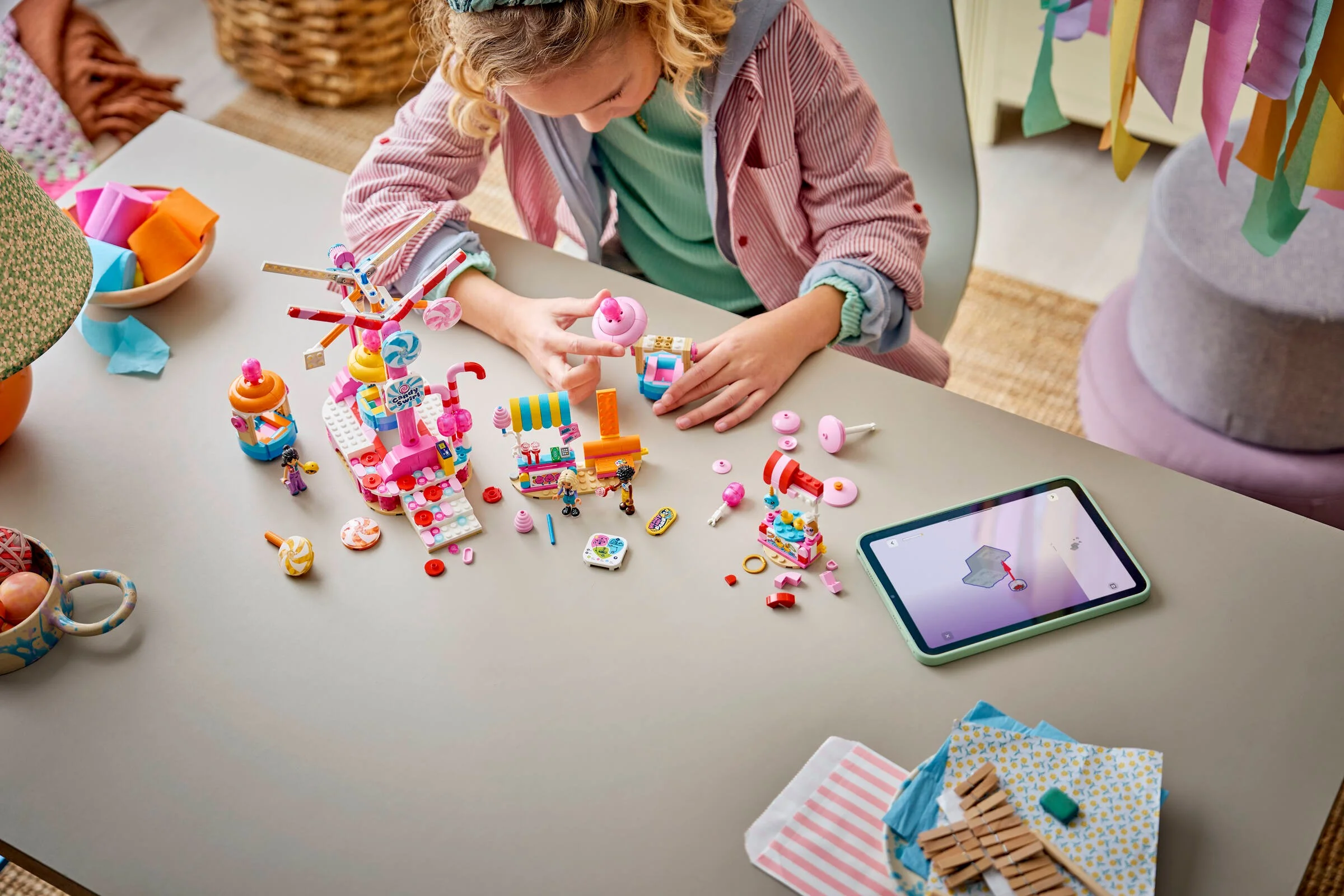 Fetiță construind roata Ferris cu dulciuri și brioșe LEGO Friends, urmând instrucțiunile de pe tabletă.