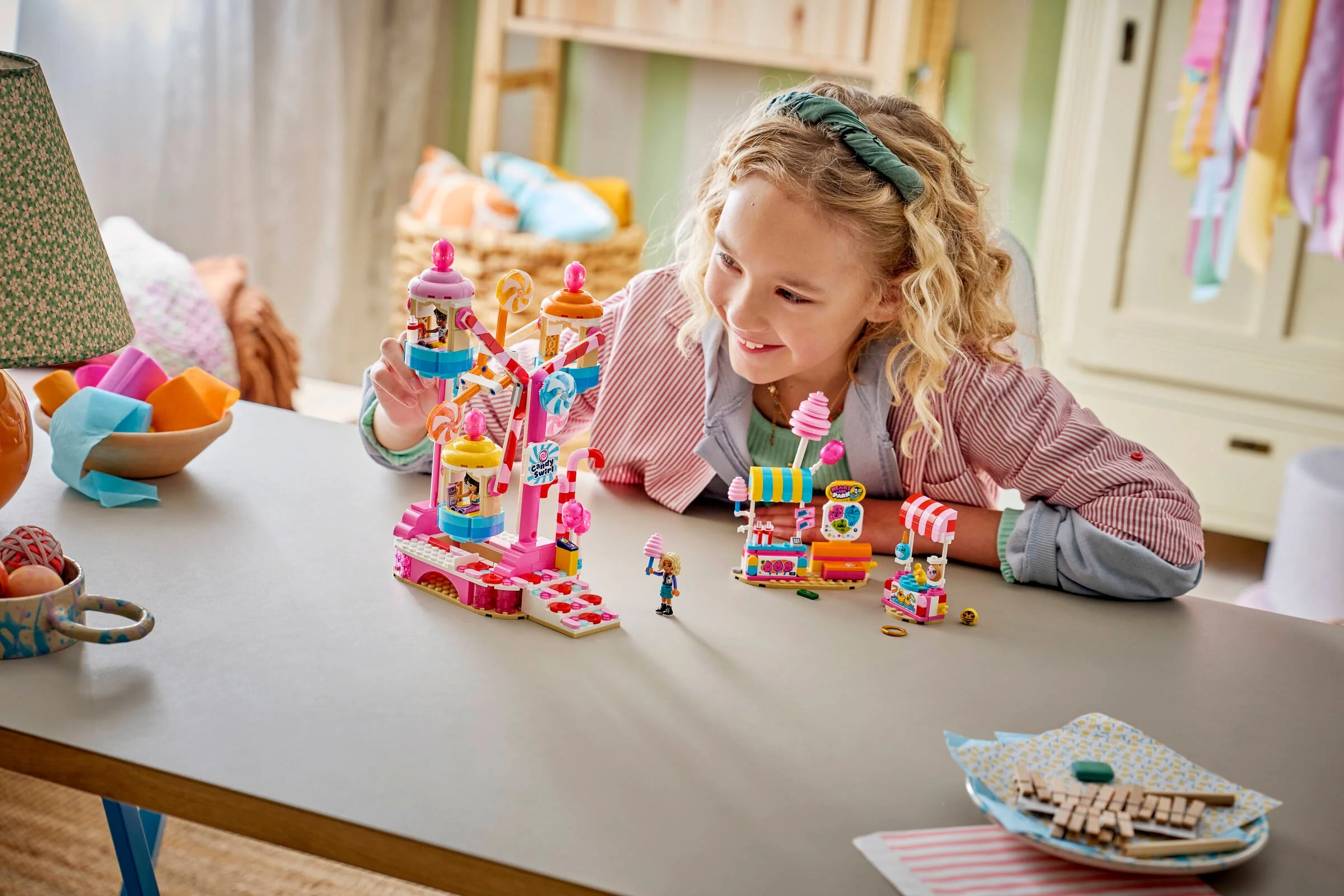 Fetiță zâmbitoare se joacă cu roata Ferris și standurile de dulciuri LEGO Friends.