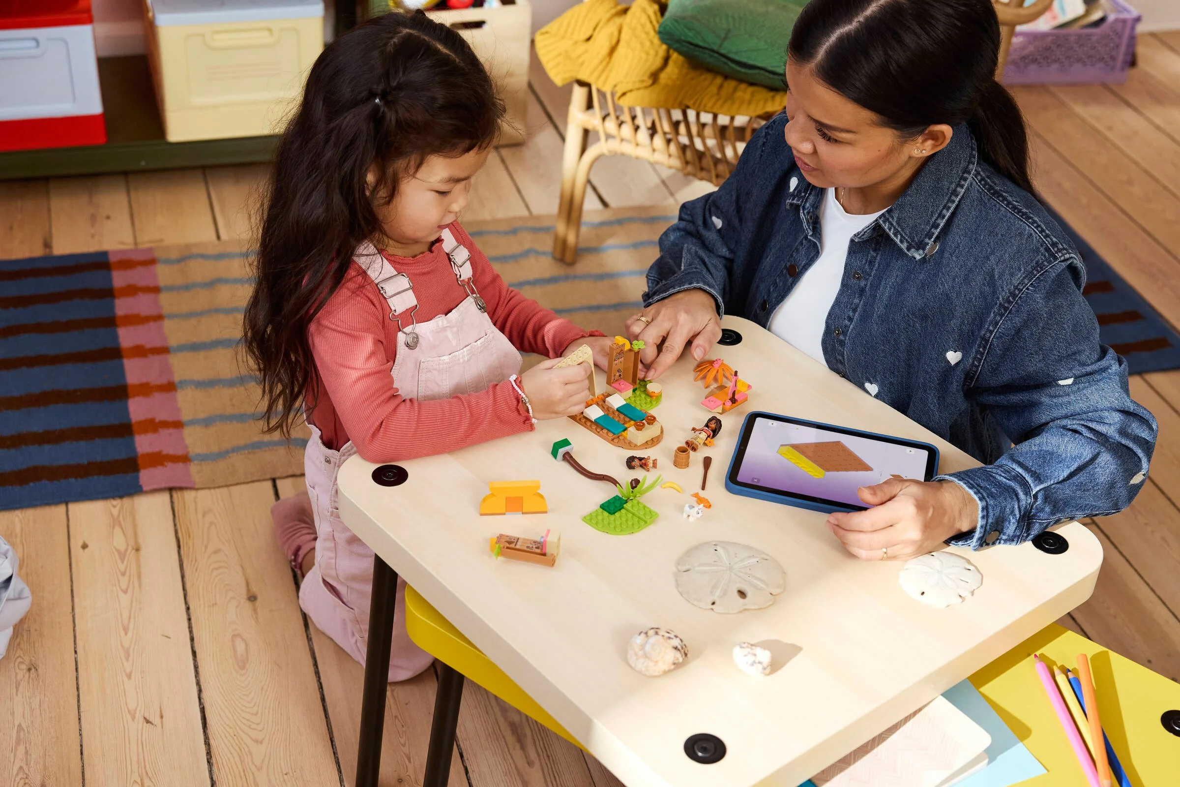 O fetiță și mama construiesc setul LEGO Disney Moana 43282 împreună, urmând instrucțiunile de pe tabletă.