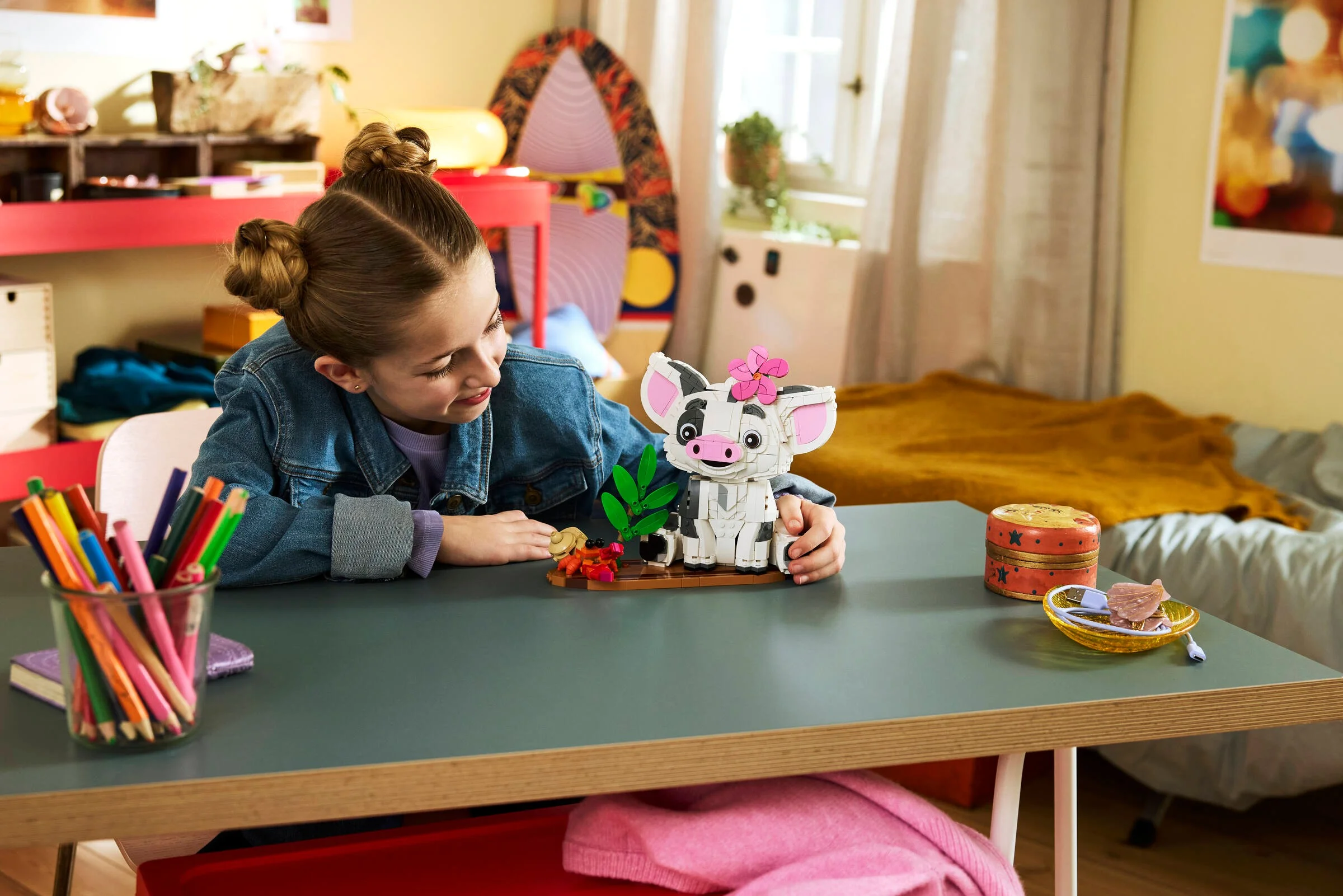 O fată interacționează cu modelul LEGO Pua, zâmbind și examinându-l atent.