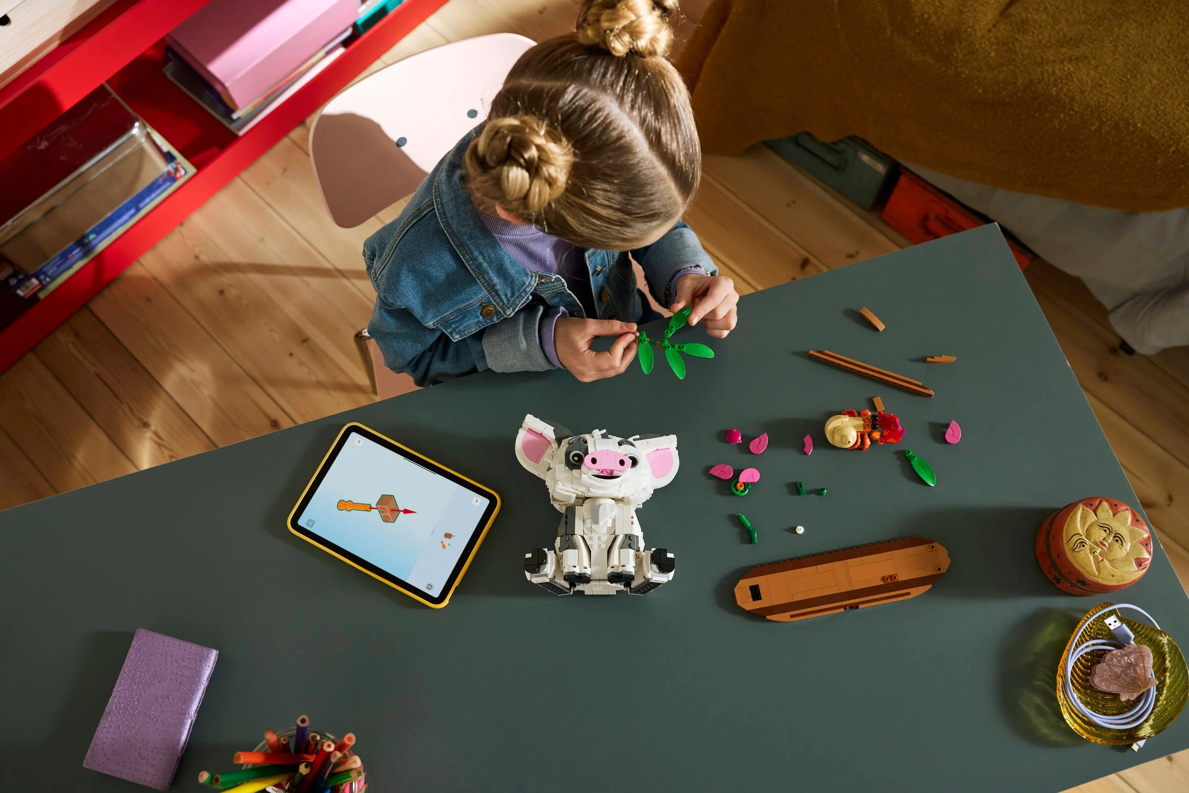O fetiță construiește setul LEGO Pua, urmând instrucțiunile pe tabletă.