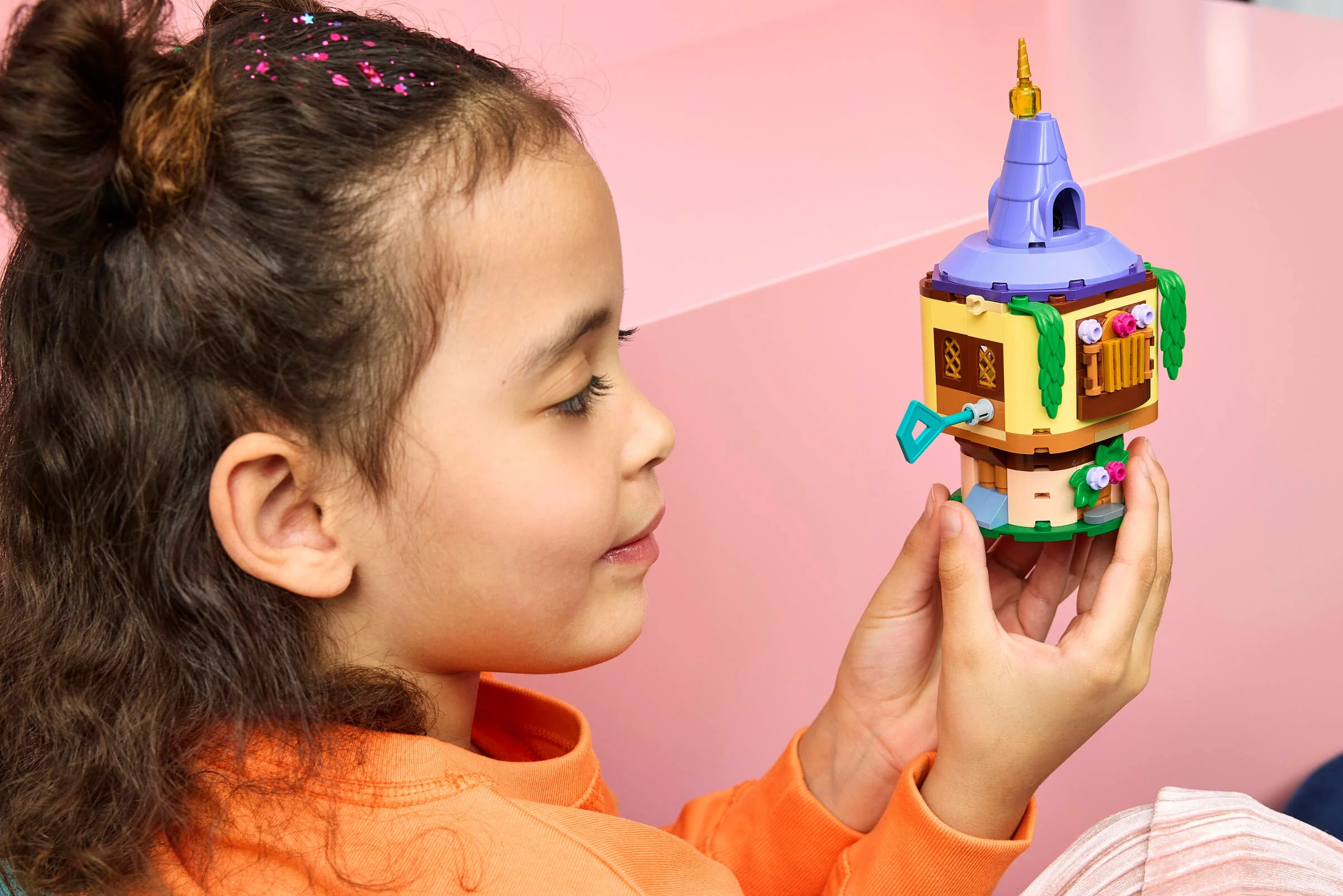 O fetiță se uită cu atenție la mini-turnul Rapunzel din LEGO, zâmbind ușor.