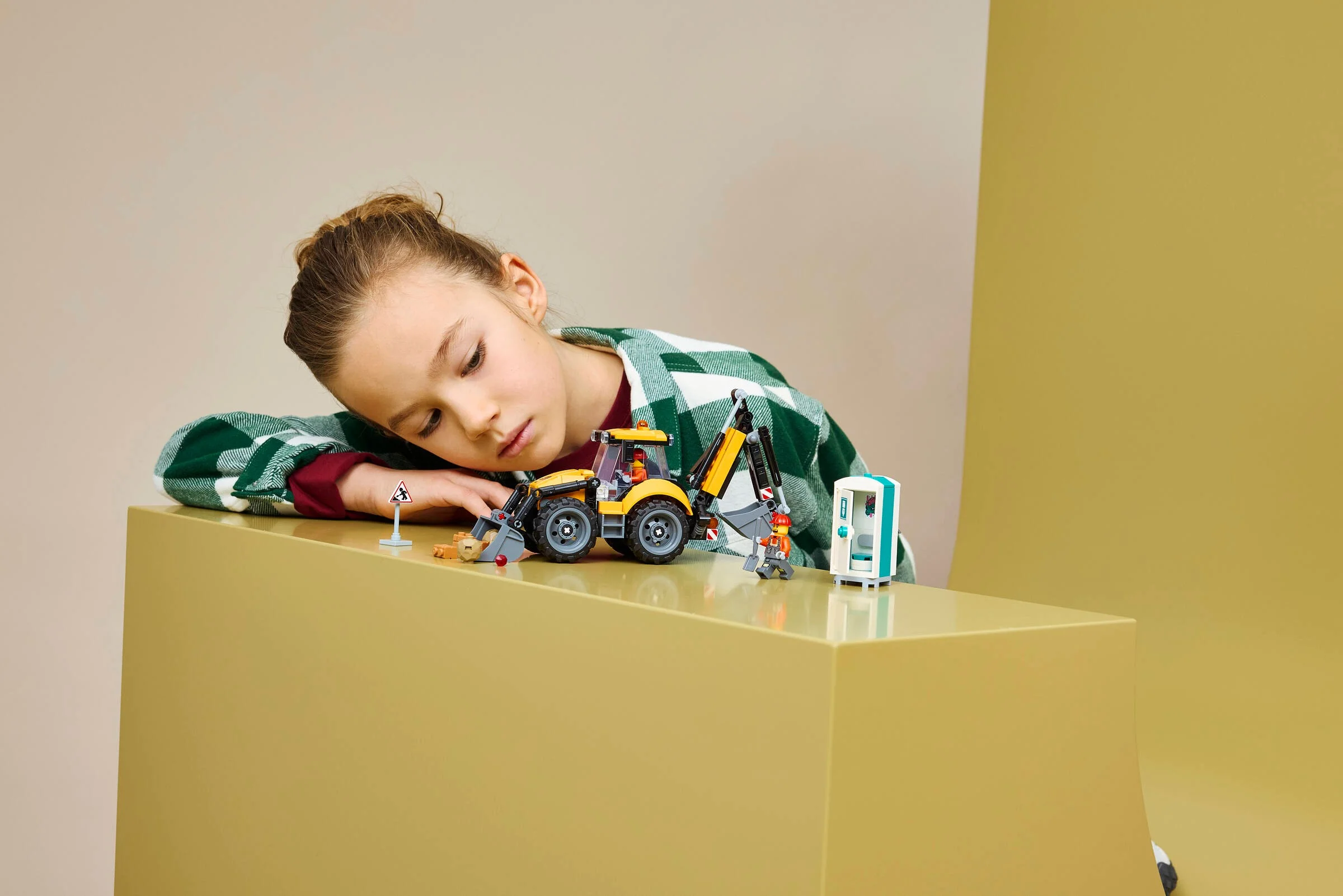 O fetiță se uită la buldoexcavatorul LEGO City 60480, cu toaletă portabilă și semn de avertizare.