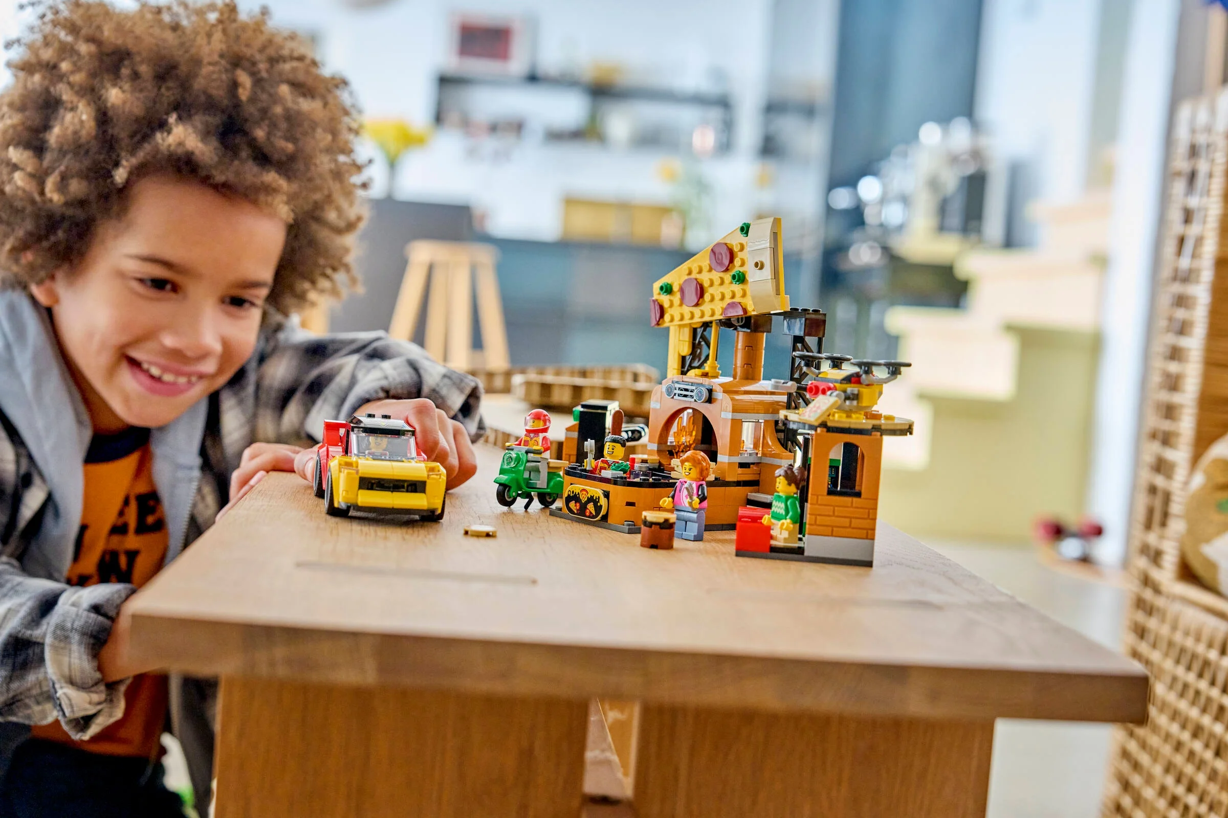 Un băiat zâmbește în timp ce se joacă cu setul LEGO Pizza Delivery Experience.