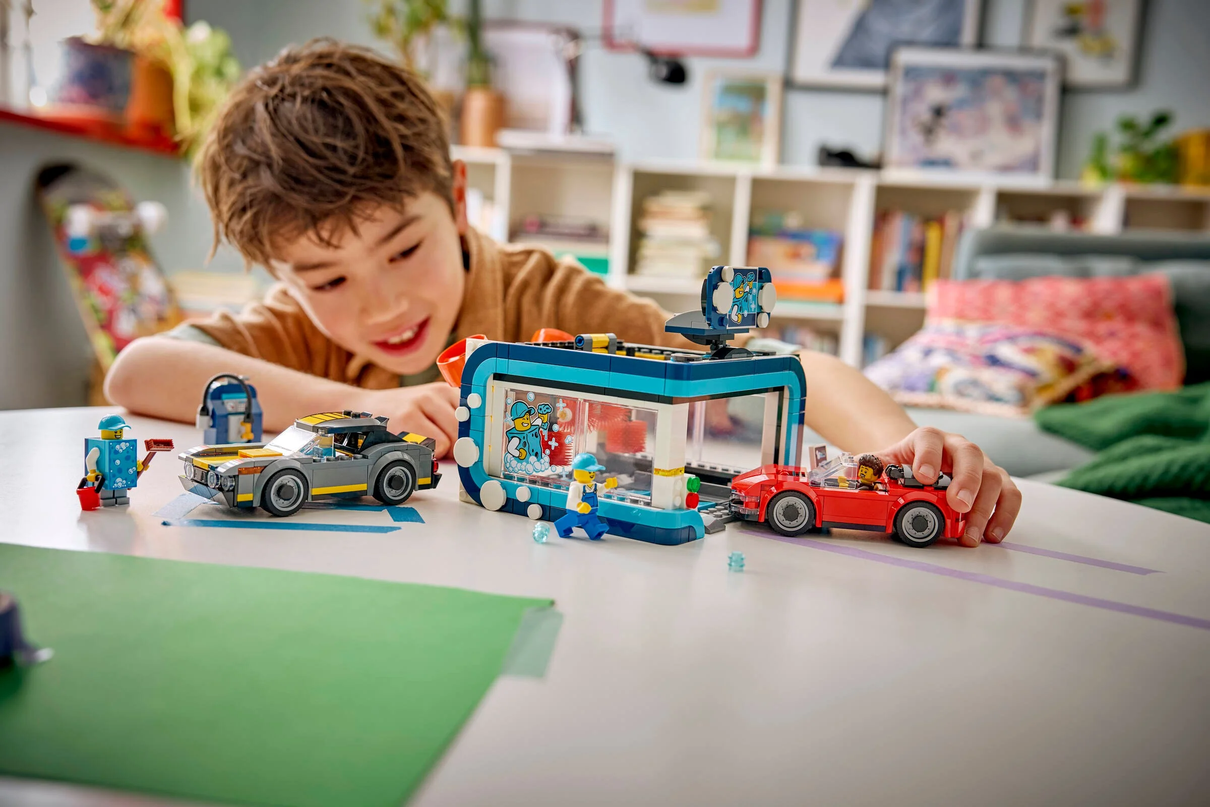 Băiat se joacă cu spălătoria auto LEGO City, cu mașini și minifigurine incluse.