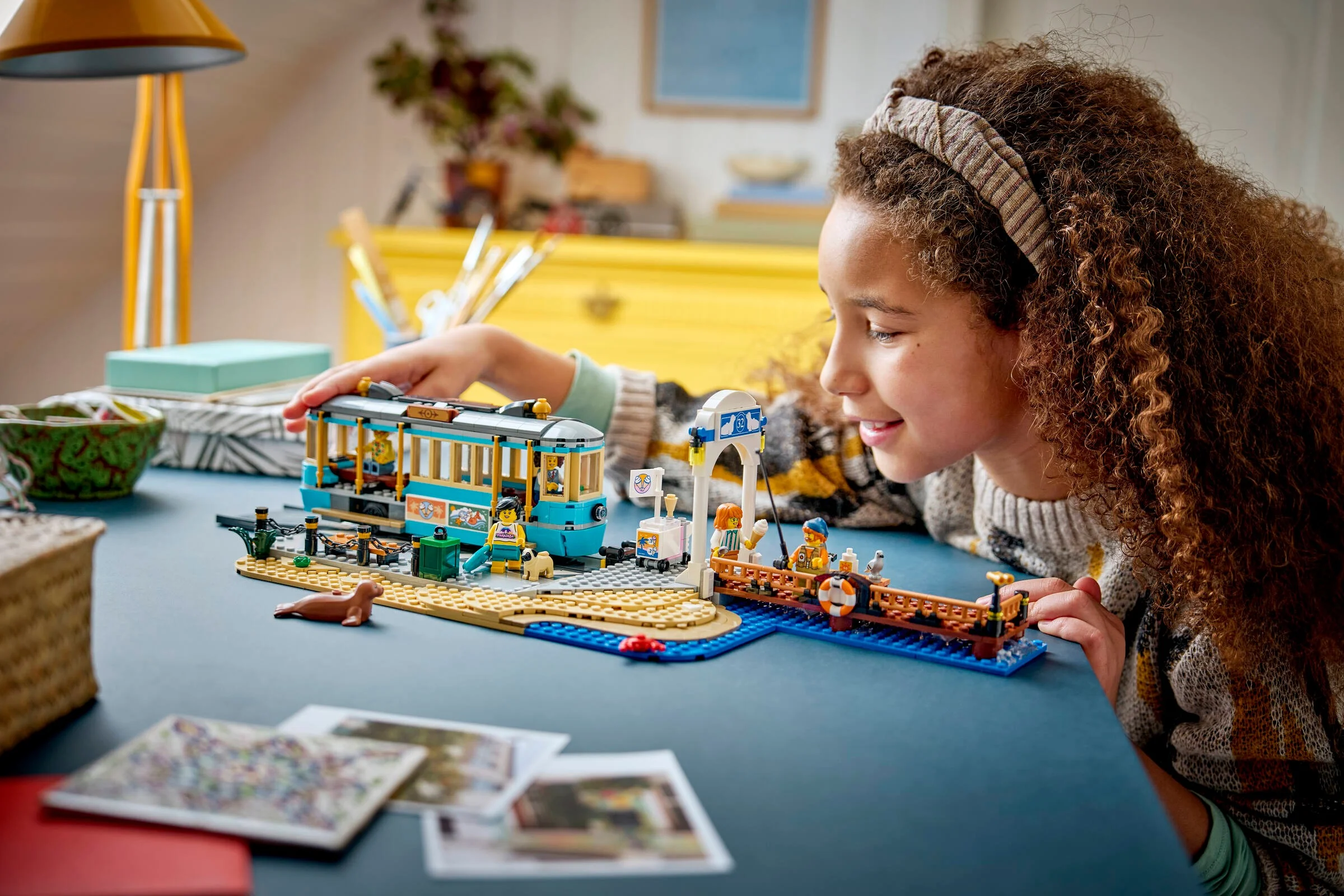 O fată se joacă cu tramvaiul de plajă LEGO, explorând detaliile și minifigurinele.