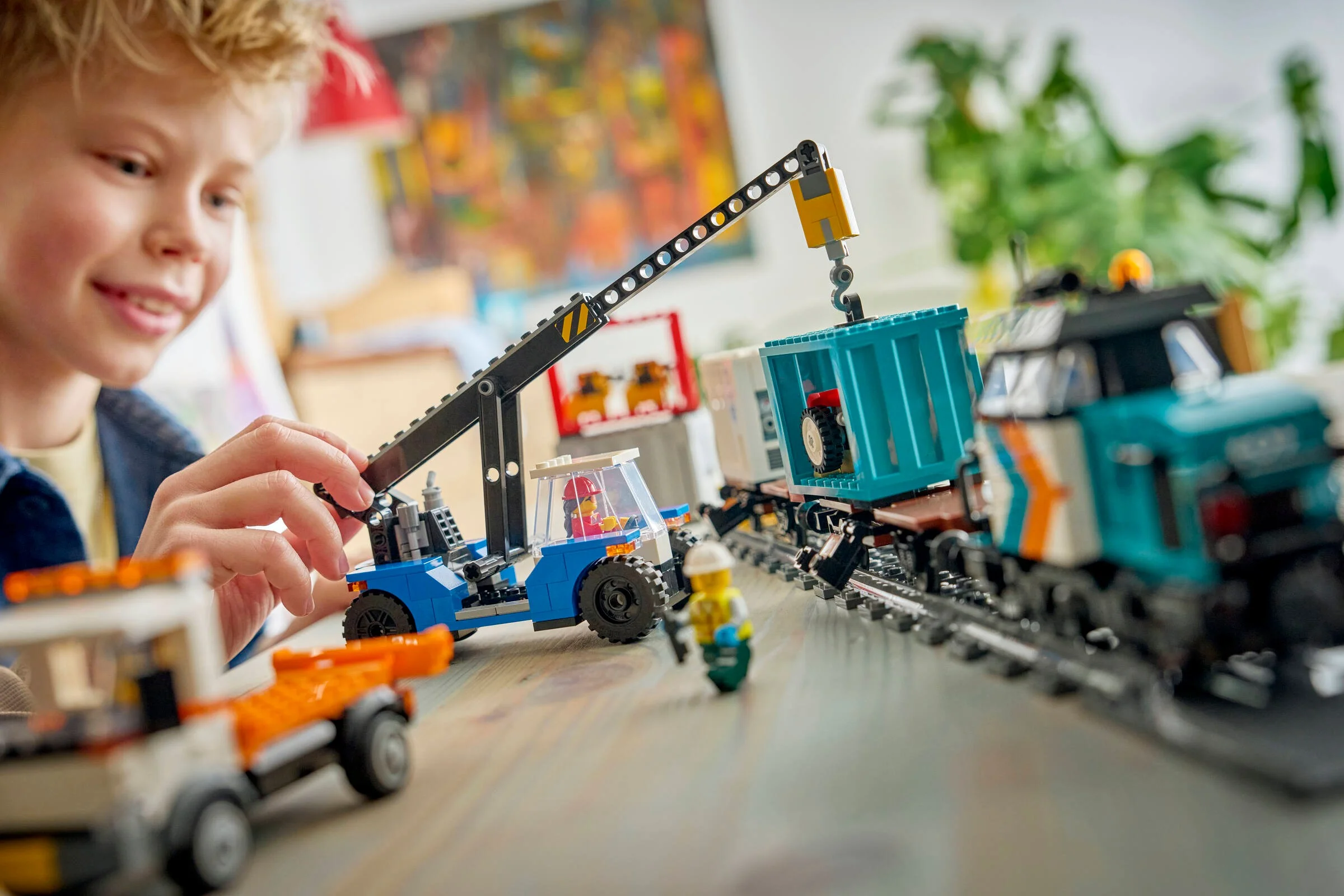 Copil se joacă cu trenul de marfă LEGO City 60509, folosind macaraua pentru a muta containere.