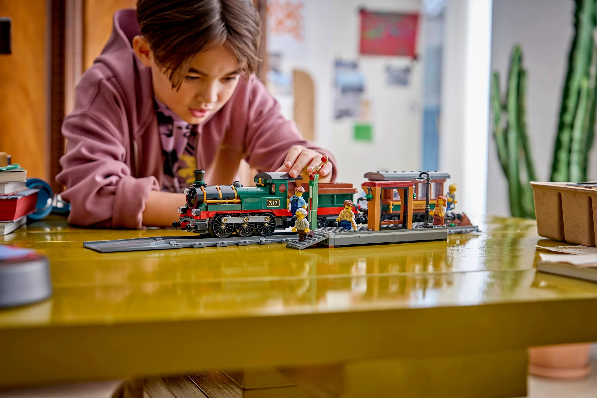 Copil interacționând cu trenul LEGO, la gară, detaliind setul și joaca.