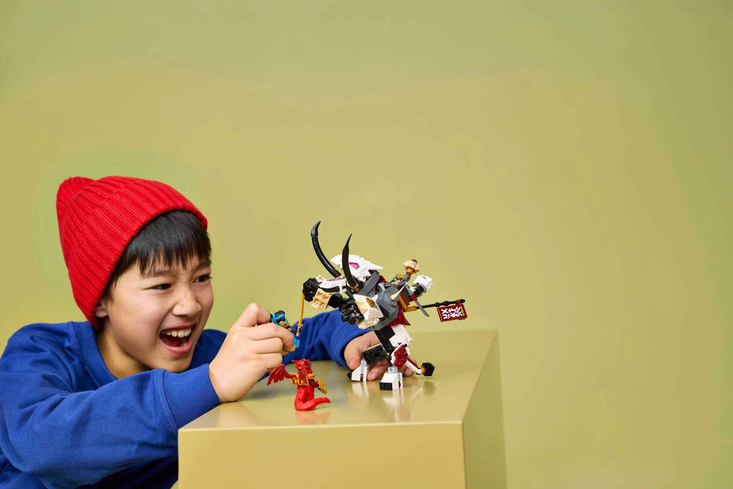 Băiat zâmbitor se joacă cu setul LEGO Ninjago Zilvar și Grimtak. Copil fericit cu jucăria sa nouă.