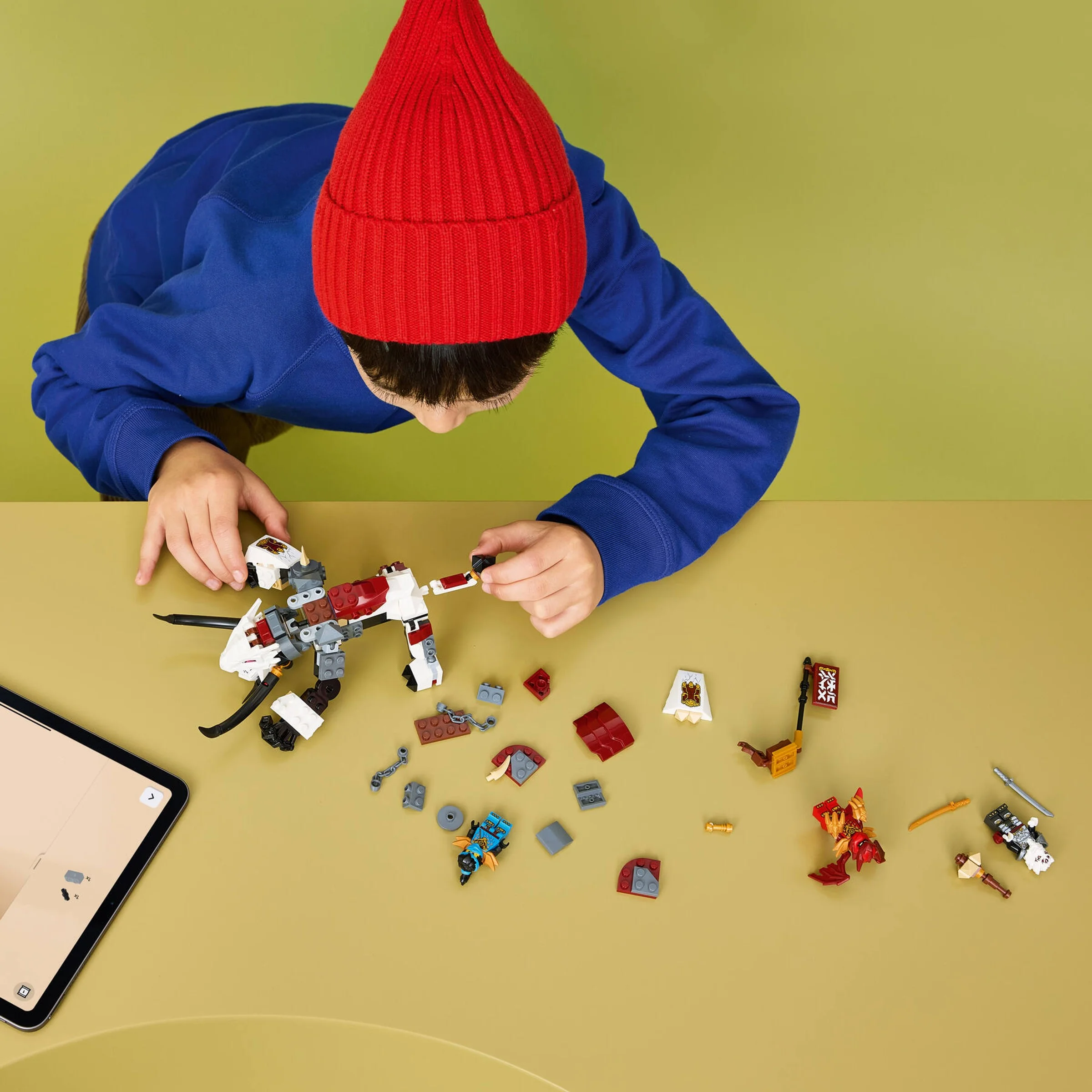 Copil construind setul LEGO Ninjago 71863, Zilvar și Grimtak, urmând instrucțiunile de pe tabletă.