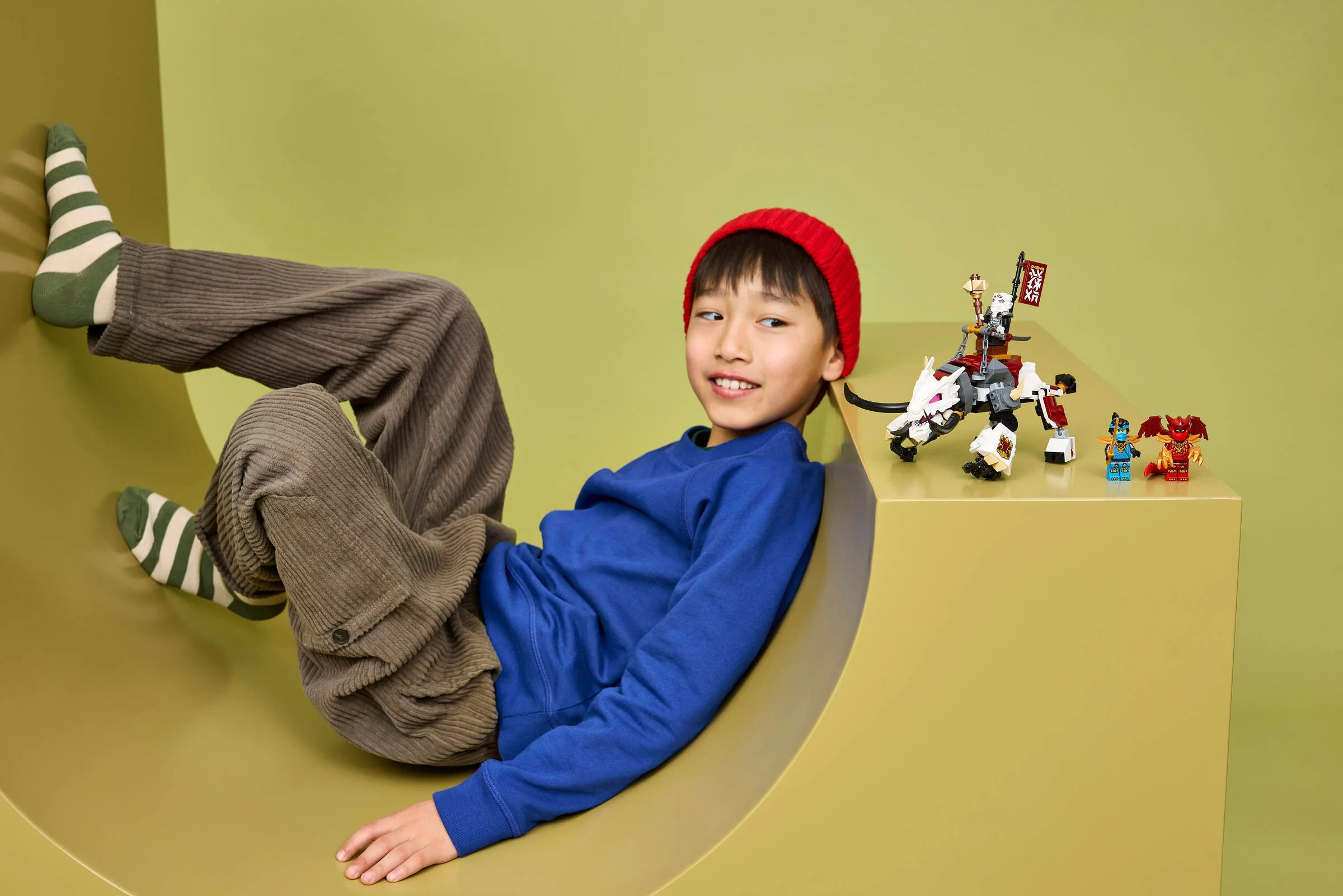 Copil zâmbitor lângă Zilvar și Grimtak, jucării LEGO Ninjago. Imagine de prezentare a produsului.