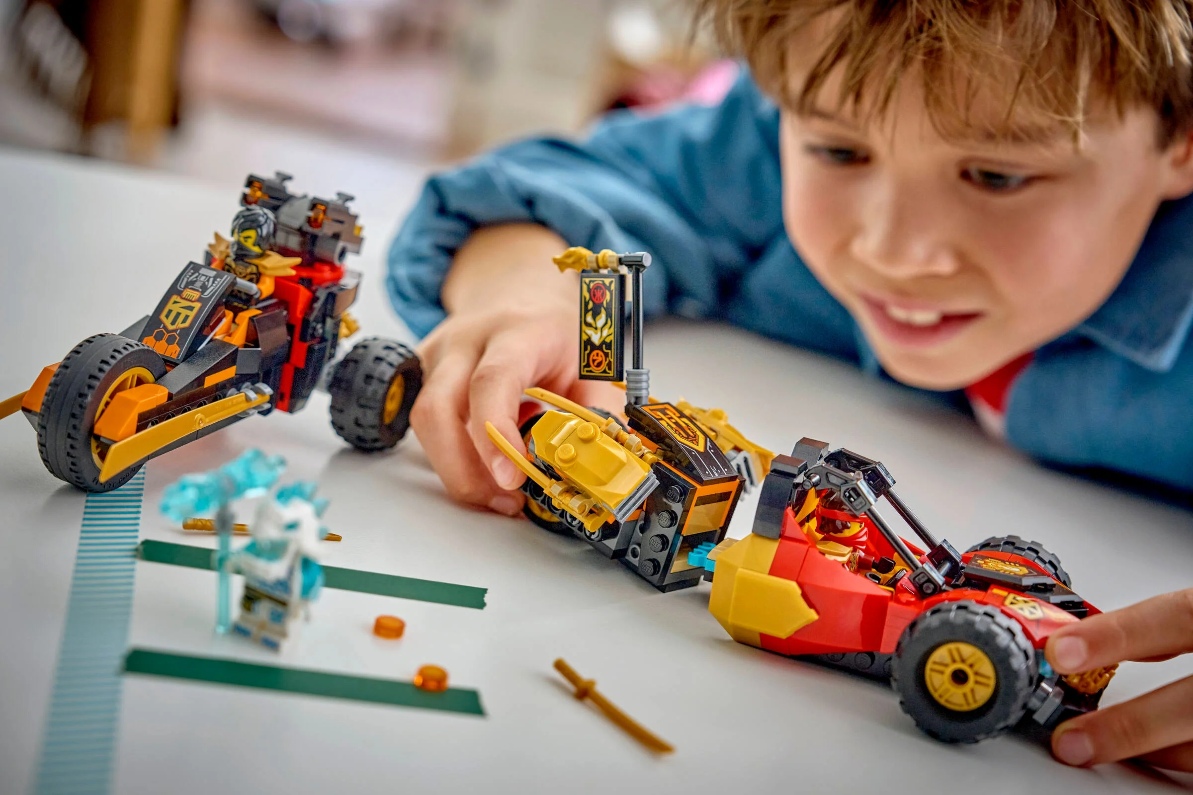 Băiat se joacă cu setul LEGO Ninjago cu vehiculele lui Kai și Cole.