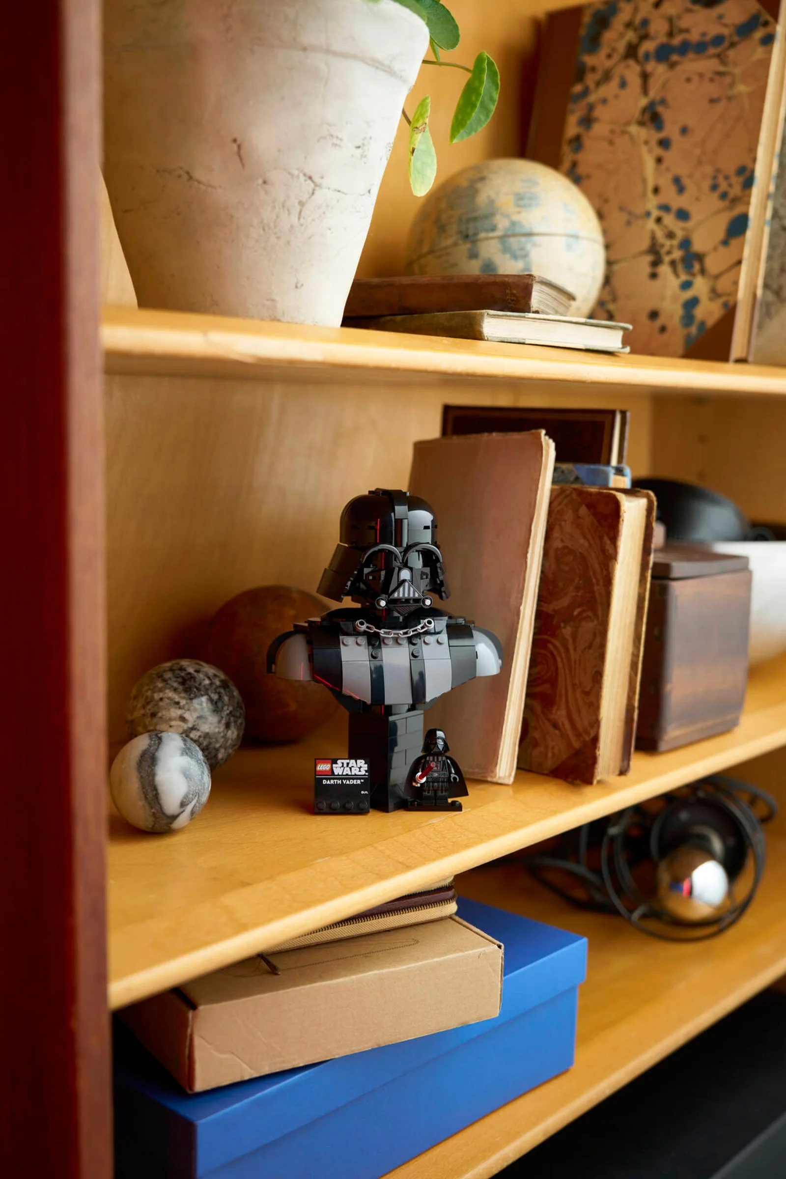 Bustul LEGO Darth Vader pe un raft, printre cărți și alte obiecte. O prezentare interesantă a modelului.