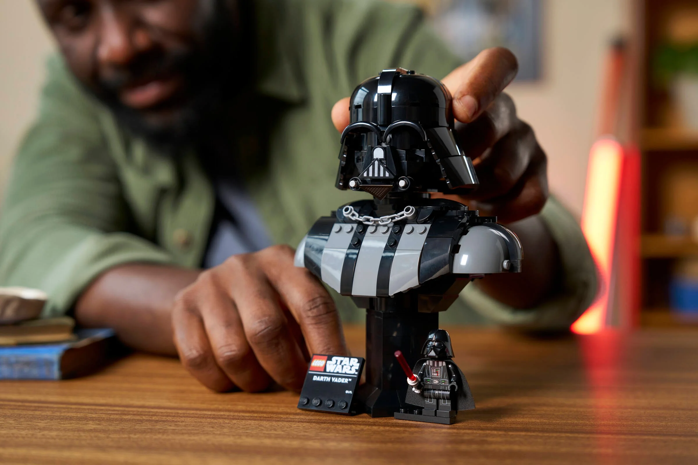 Prim-plan bustului Darth Vader LEGO, cu un adult care îi ajustează casca.