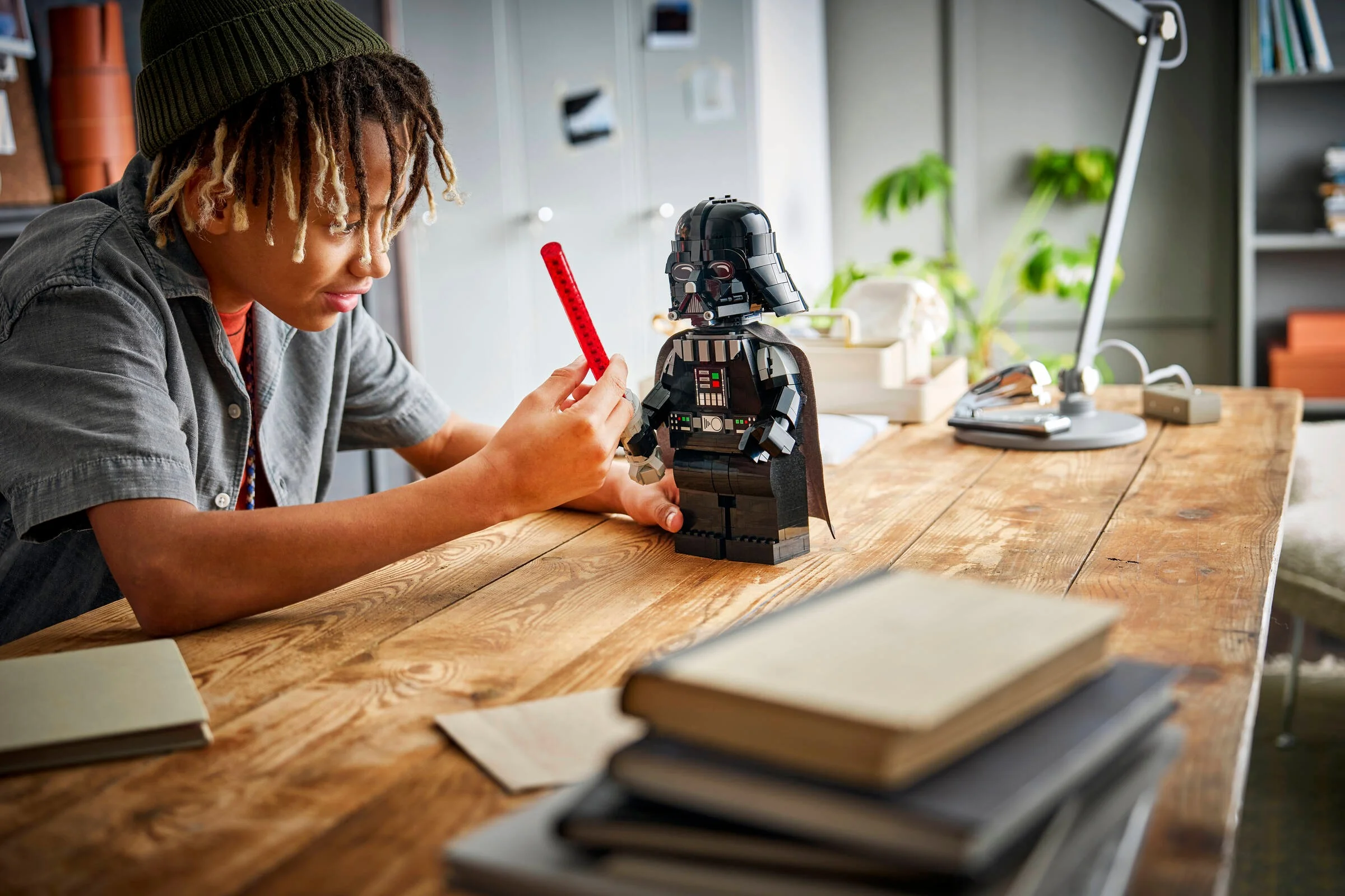 Băiat interacționând cu o figurină LEGO mărită Darth Vader, cu o sabie laser roșie.