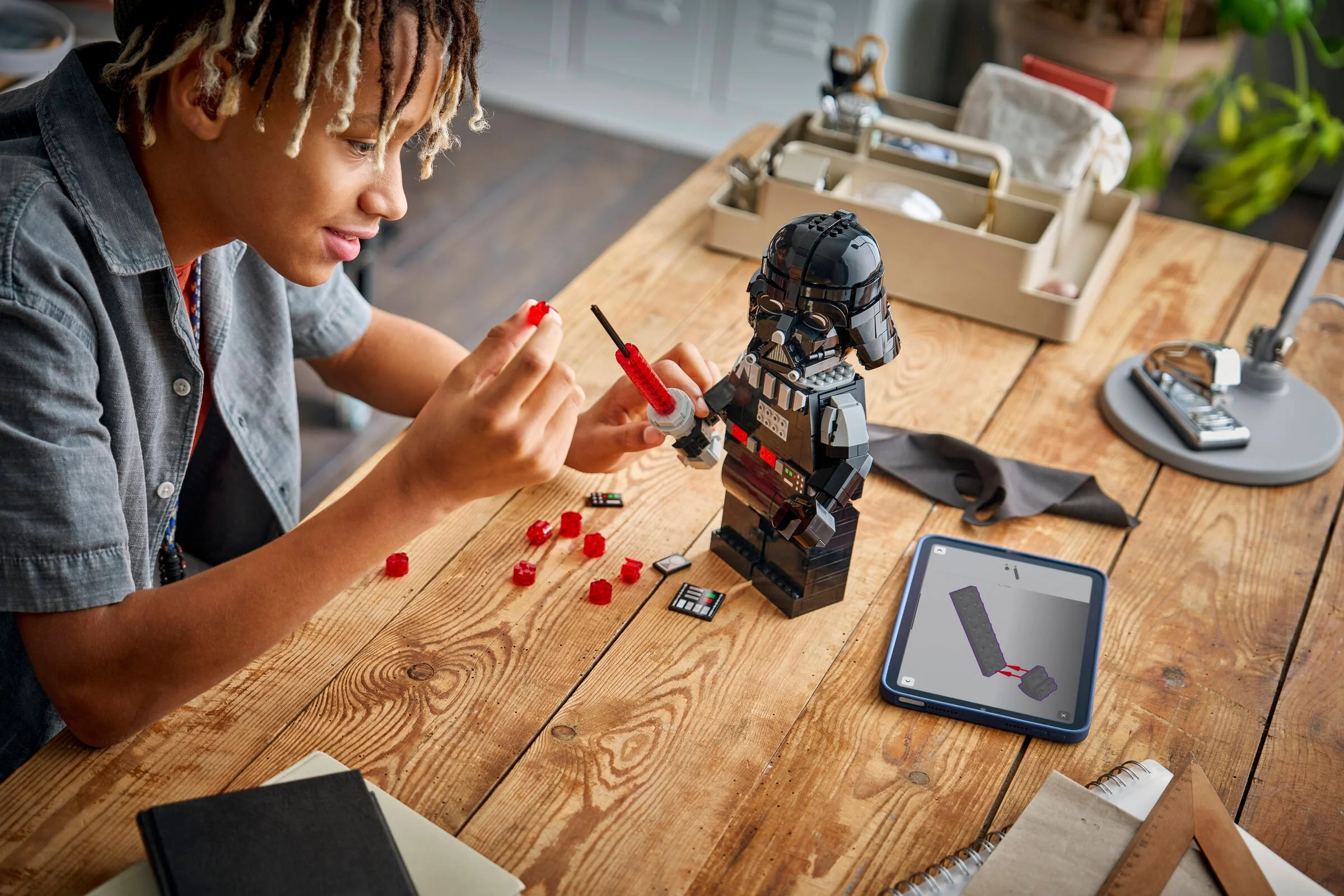 Un tânăr construiește figurina Darth Vader LEGO. Instrucțiuni digitale pe tabletă. Atmosferă creativă și relaxată.