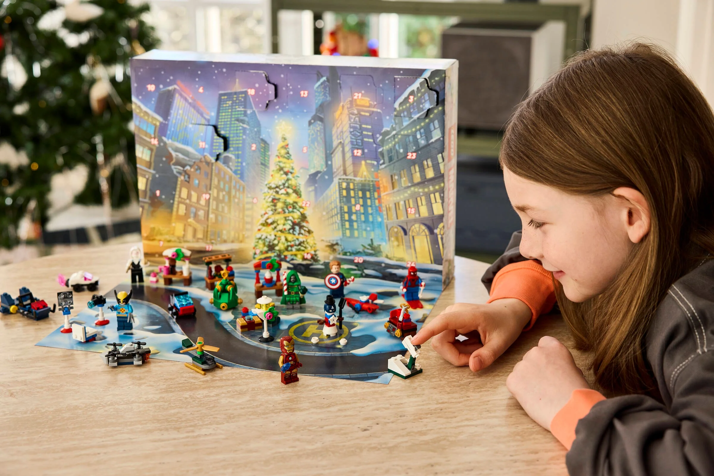 Imagine cu calendarul de advent LEGO Marvel 2026, deschis, cu o fetiță jucându-se cu minifigurinele.