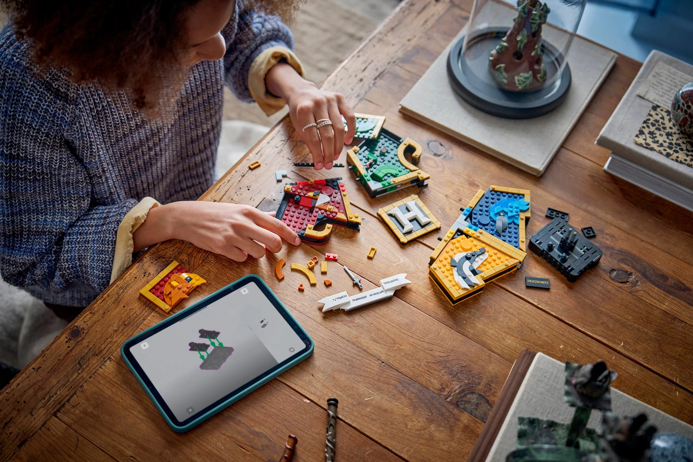 O persoană construiește crestele caselor Hogwarts cu cărămizi LEGO.
