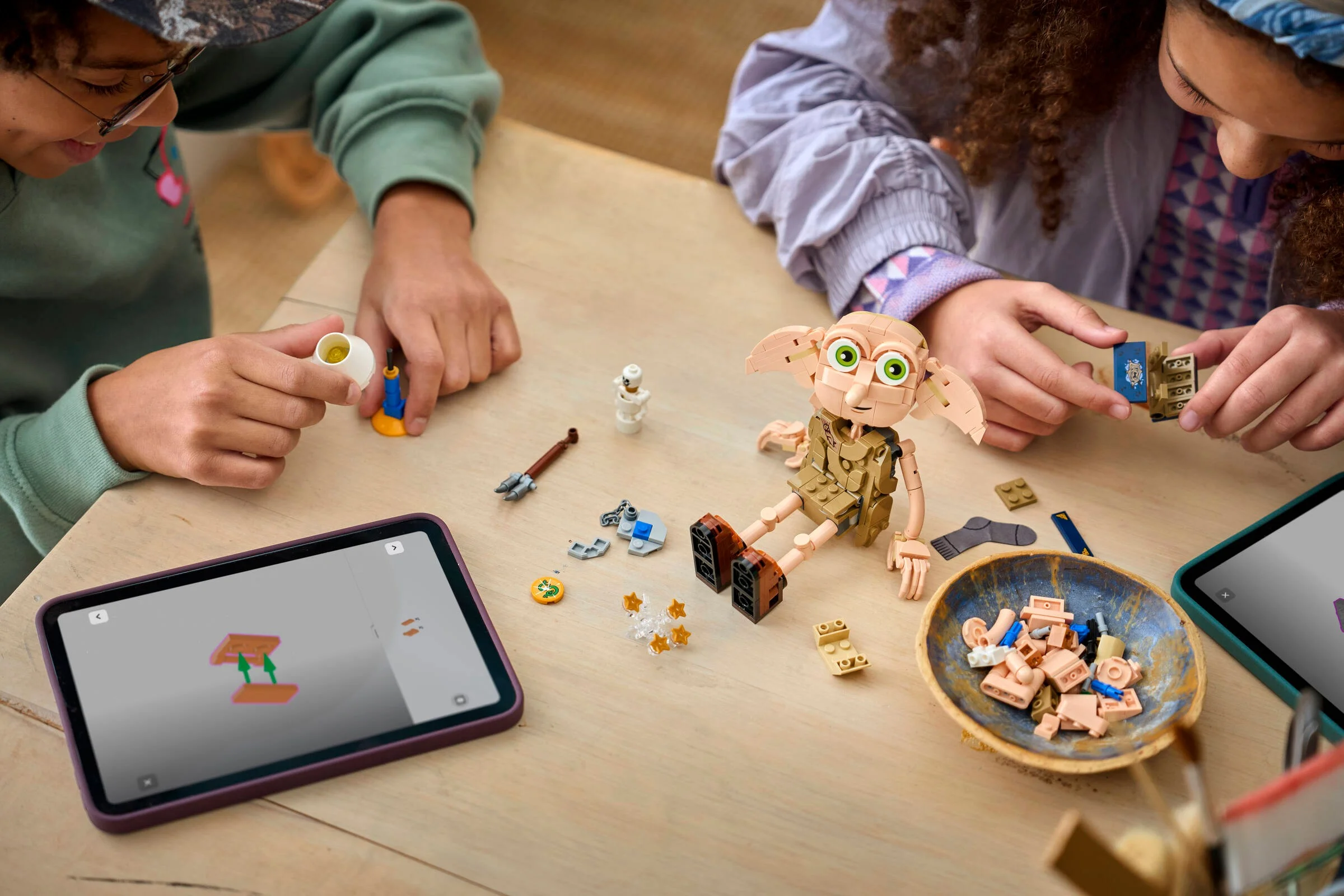 Copii construind setul LEGO Dobby, folosind instrucțiuni digitale pe tabletă.