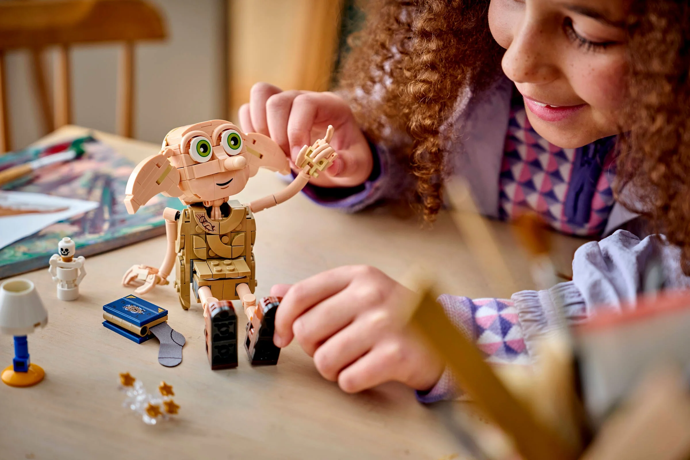 Imagine cu Dobby construit din LEGO, cu o fată interacționând. O scenă drăguță și simpatică.