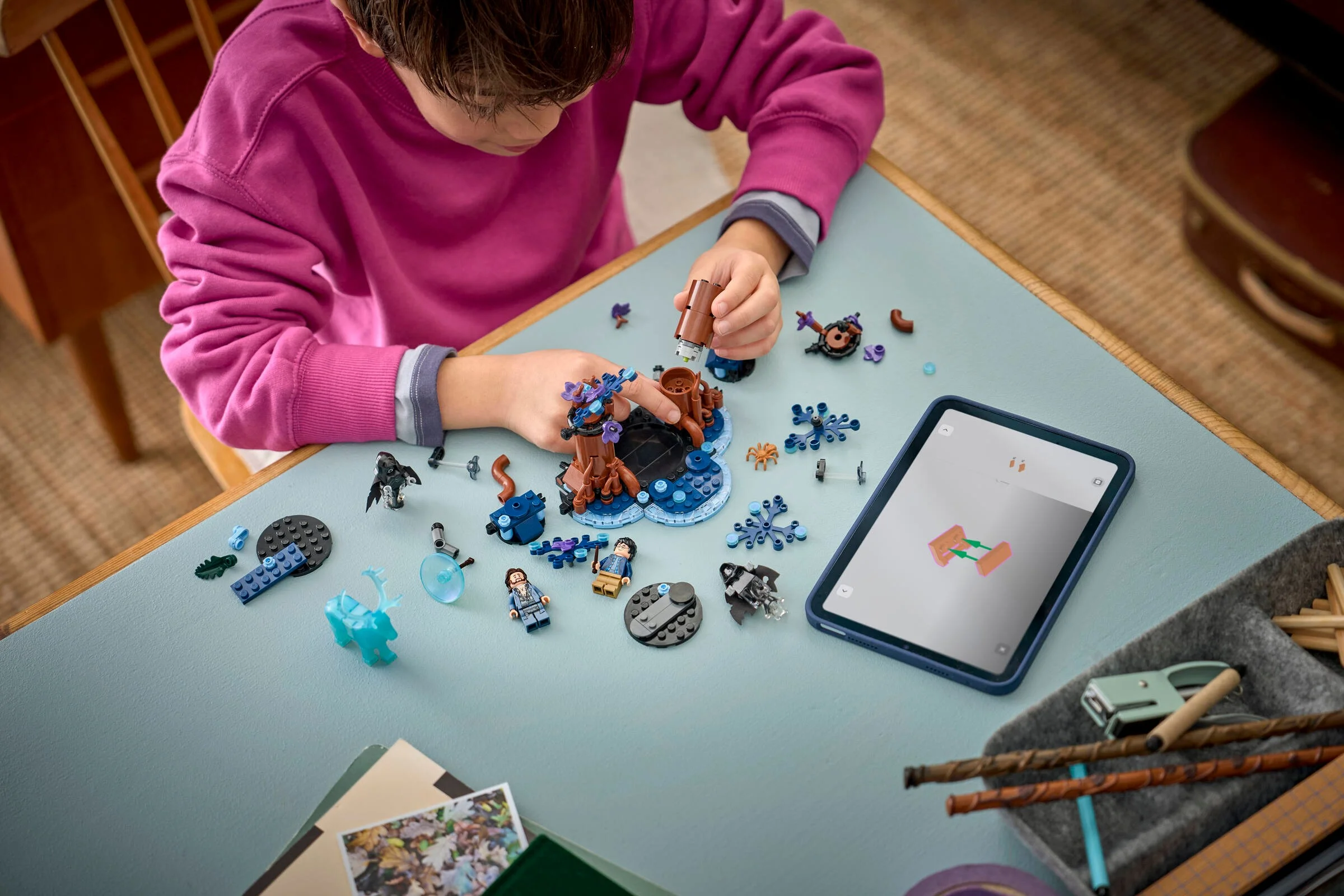 Copil construind setul LEGO Pădurea Interzisă, asistat de instrucțiuni digitale pe tabletă.