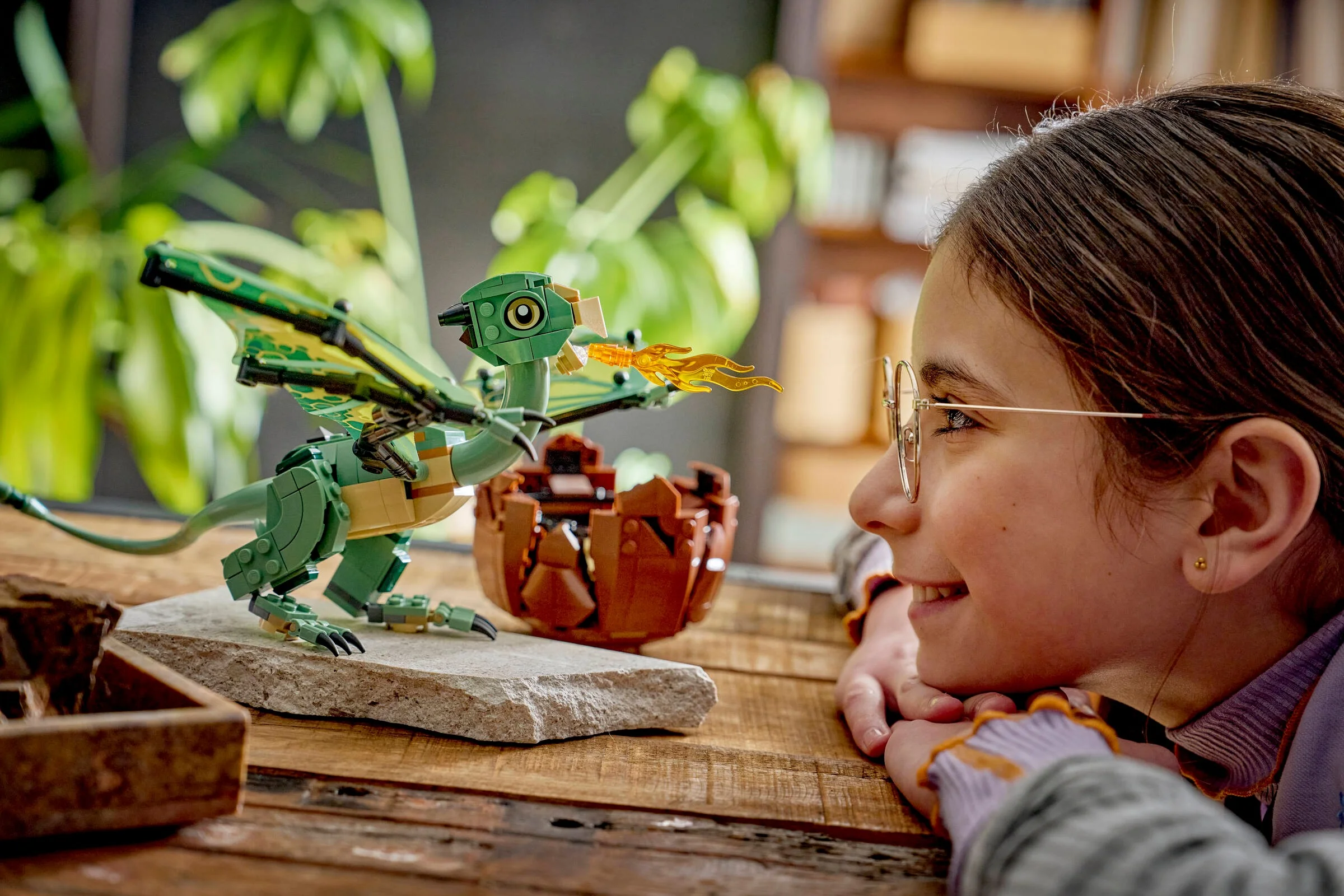 O fată admiră dragonul Norbert LEGO, stând pe o stâncă lângă un ou spart. Atmosferă magică.
