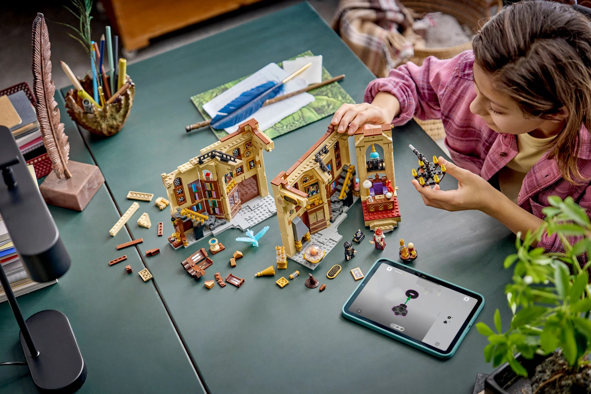 Copil construind setul LEGO 76478, Biroul lui Dumbledore, pe o masă verde. Setul este parțial asamblat.