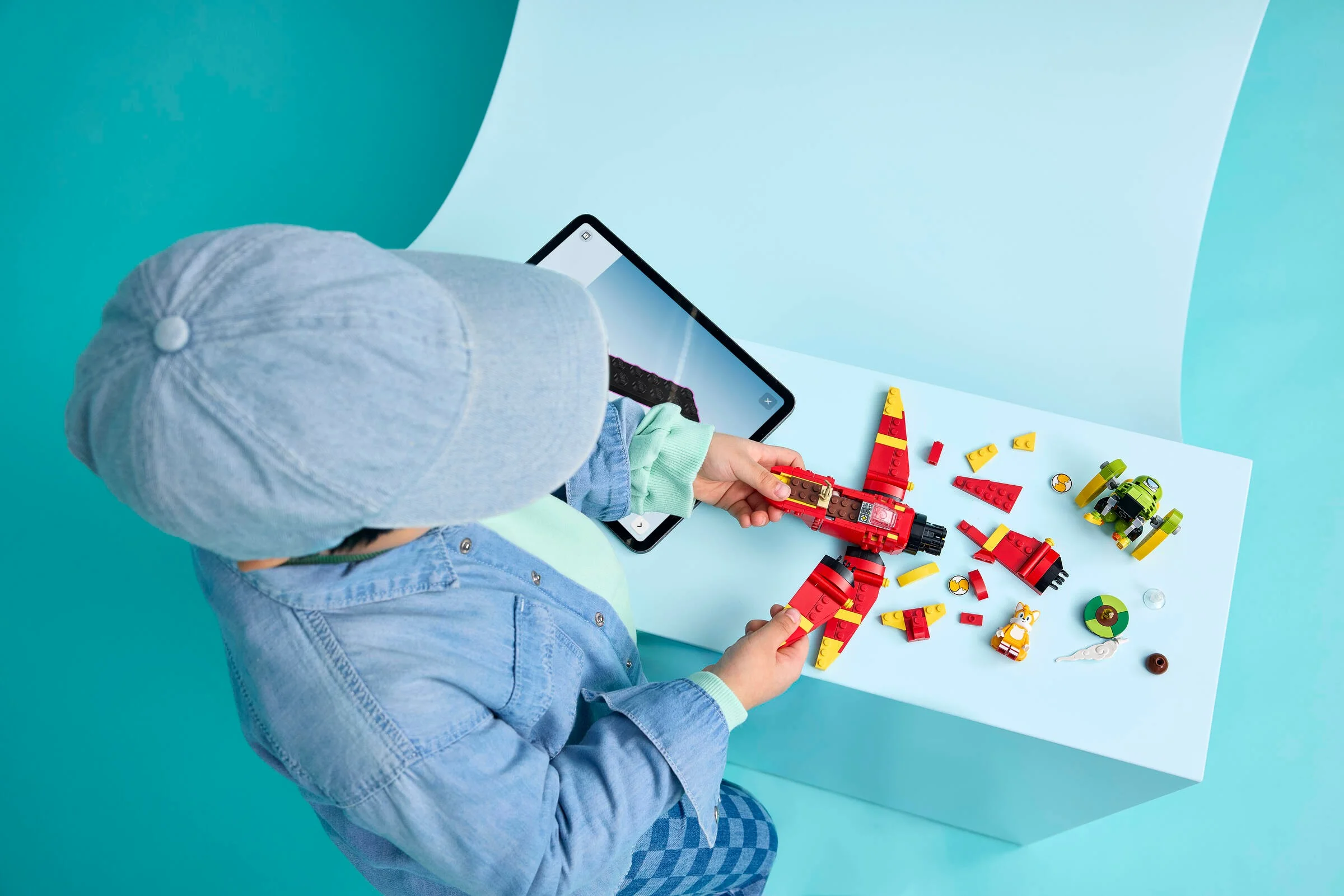 Copil construind avionul Tails' Tornado-1 cu instrucțiuni de pe tabletă. Set LEGO distractiv.