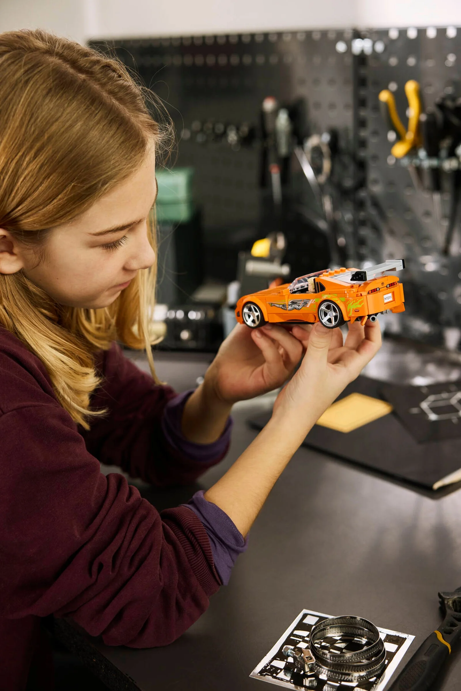 O fată admiră Toyota Supra MK4 portocalie, asamblată din LEGO, într-un atelier.