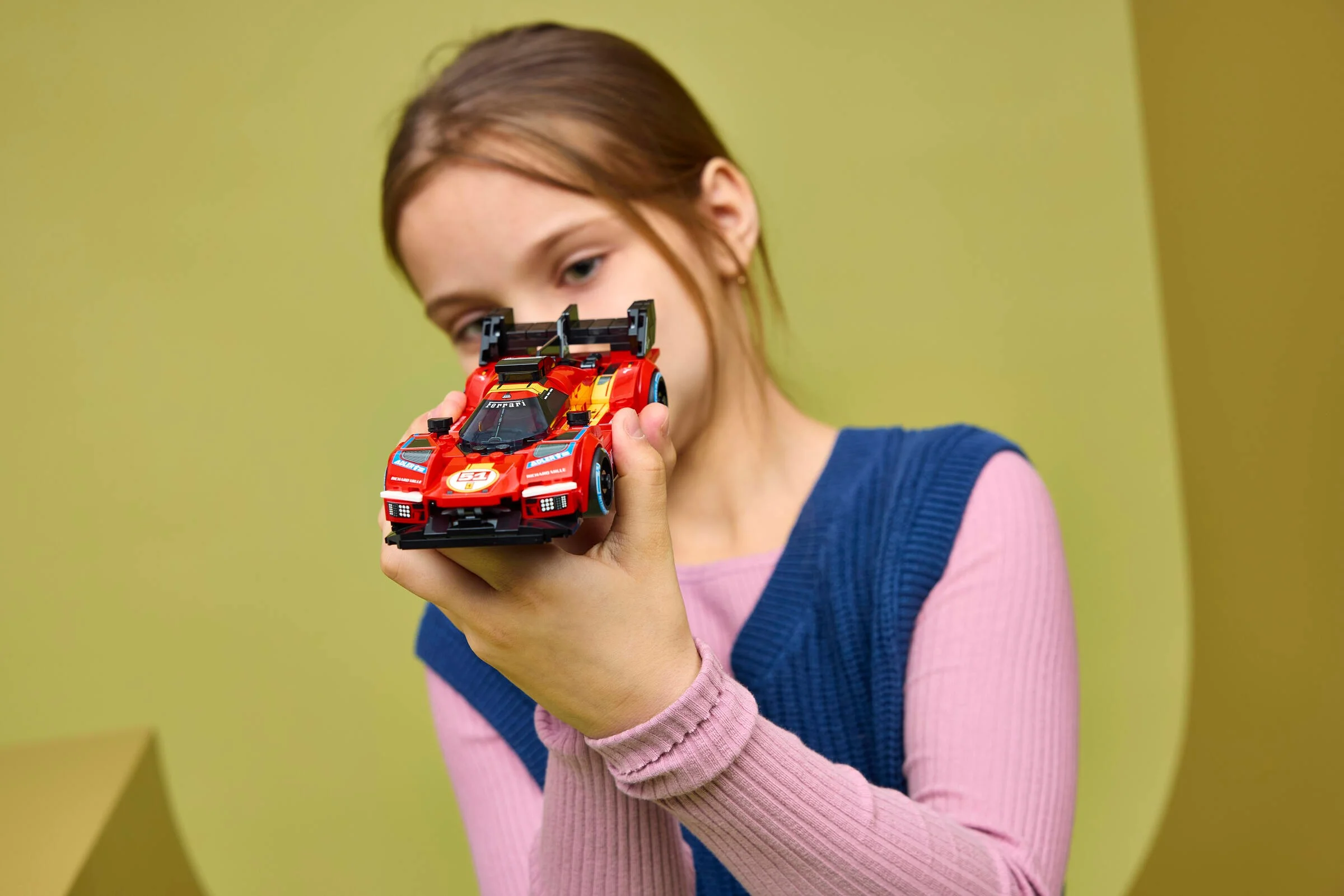 Fată ținând modelul LEGO Ferrari 499P, o jucărie detaliată și realistă.