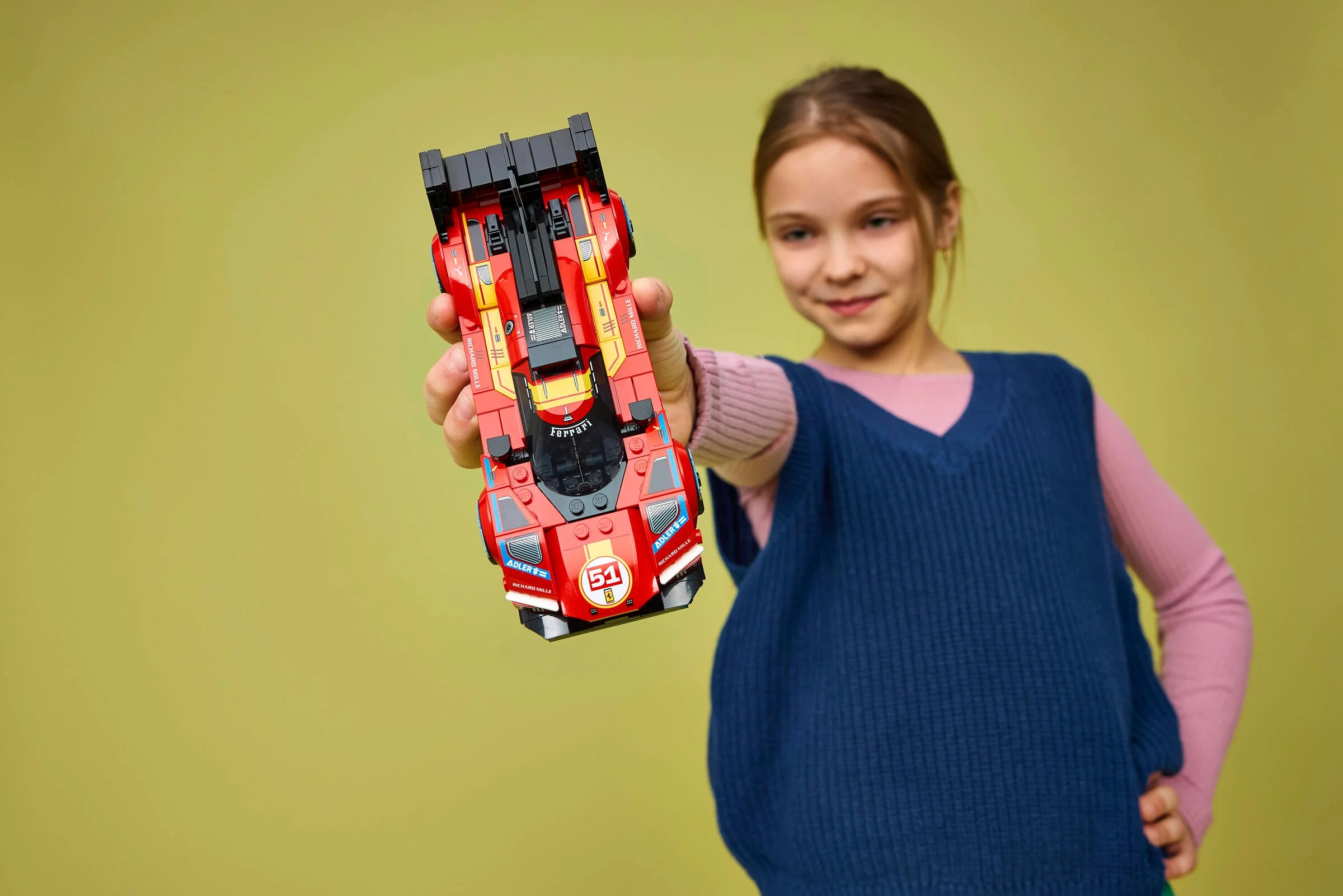 Fată zâmbitoare ținând în mână modelul LEGO Ferrari 499P, roșu și negru.