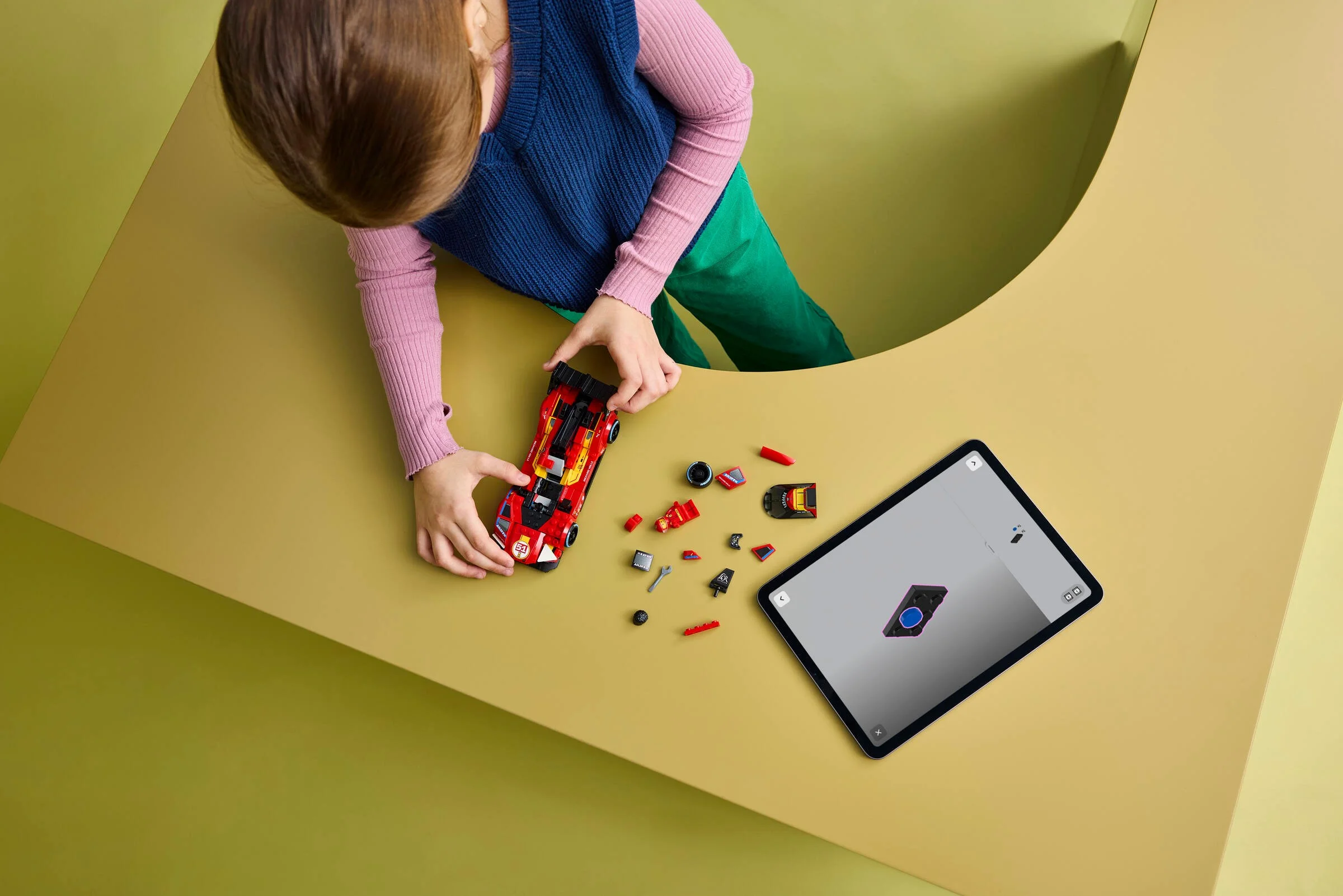 Fetiță construind mașina Ferrari 499P folosind instrucțiuni digitale pe tabletă.