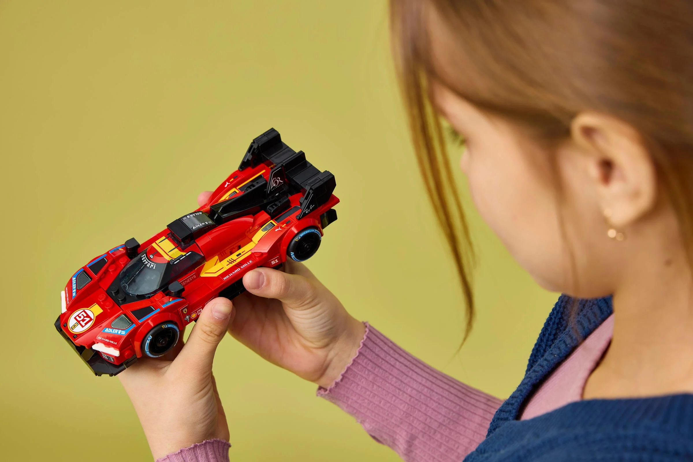 Modelul Ferrari 499P LEGO, roșu și negru, examinat de o fetiță. Detalii clare și atractive.