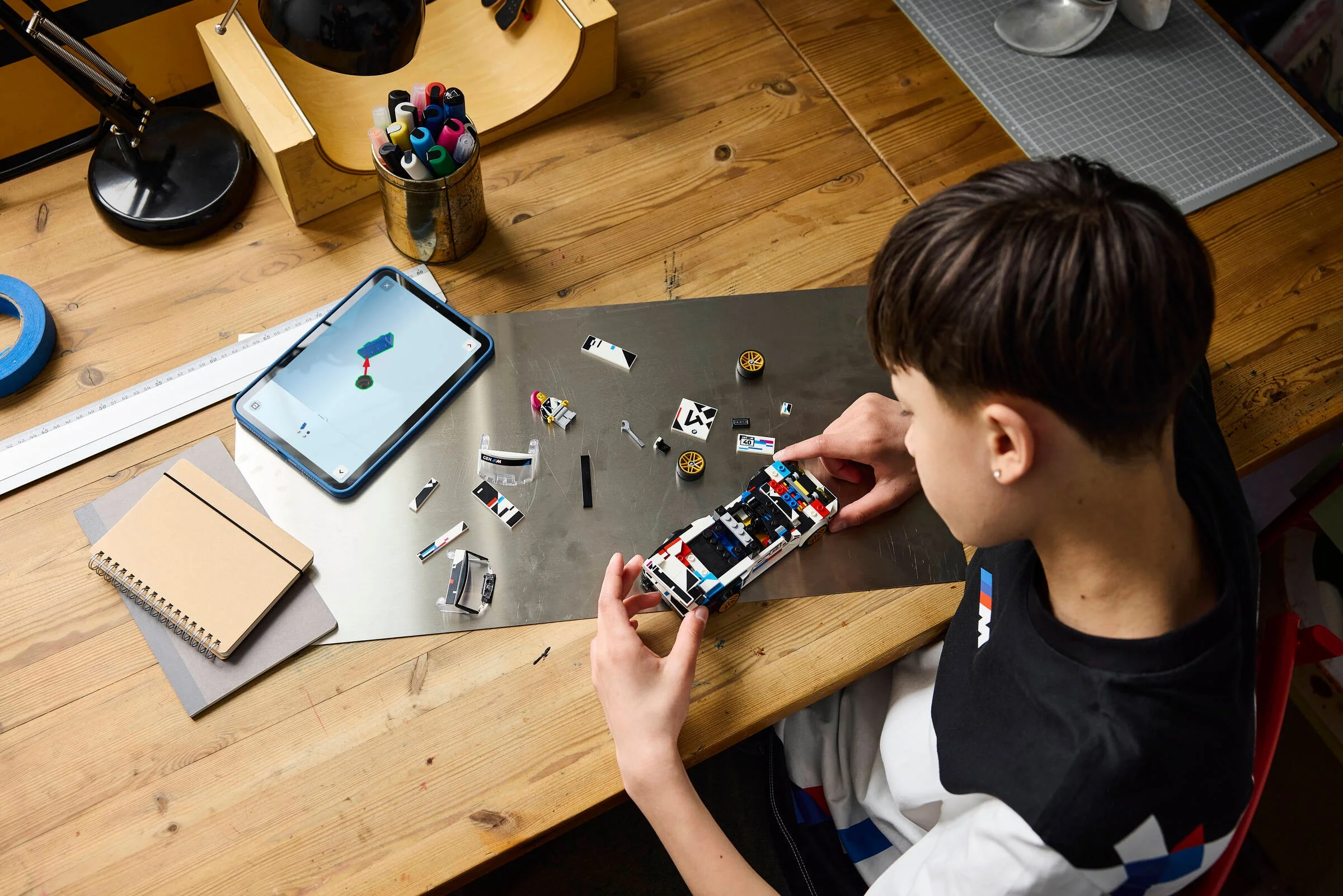 Copil asamblează modelul BMW M3 (E30) din piese LEGO, urmărind instrucțiunile digitale pe tabletă.
