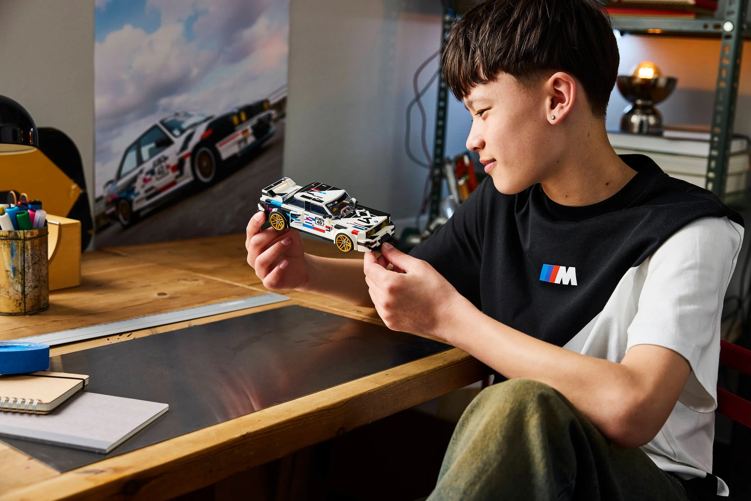 Un tânăr admiră modelul LEGO BMW M3 (E30), într-o scenă cotidiană. Detaliile mașinii sunt vizibile.