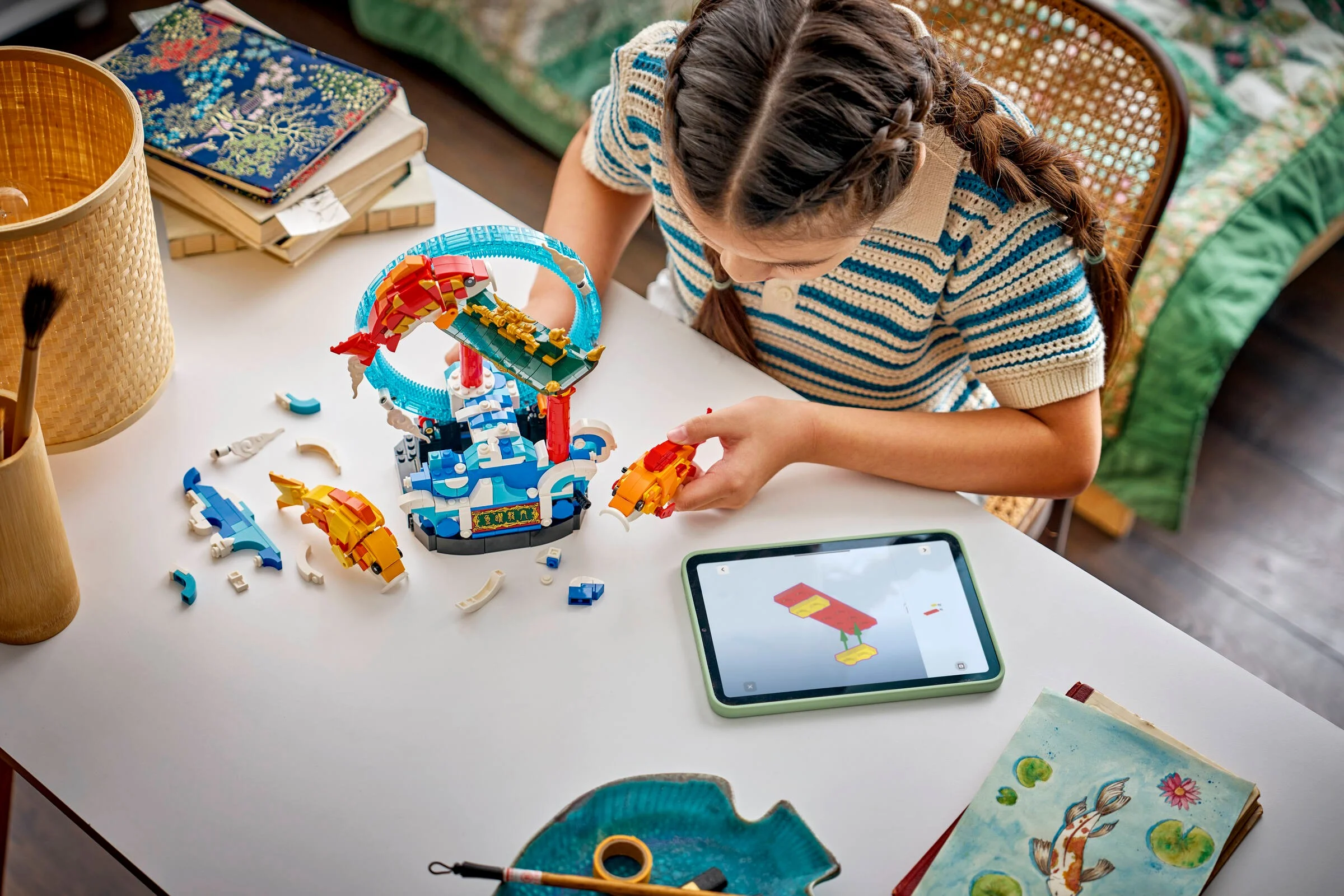 O fetiță construiește setul LEGO 80120 „Prosperity Carp Leaping” folosind instrucțiuni pe tabletă.