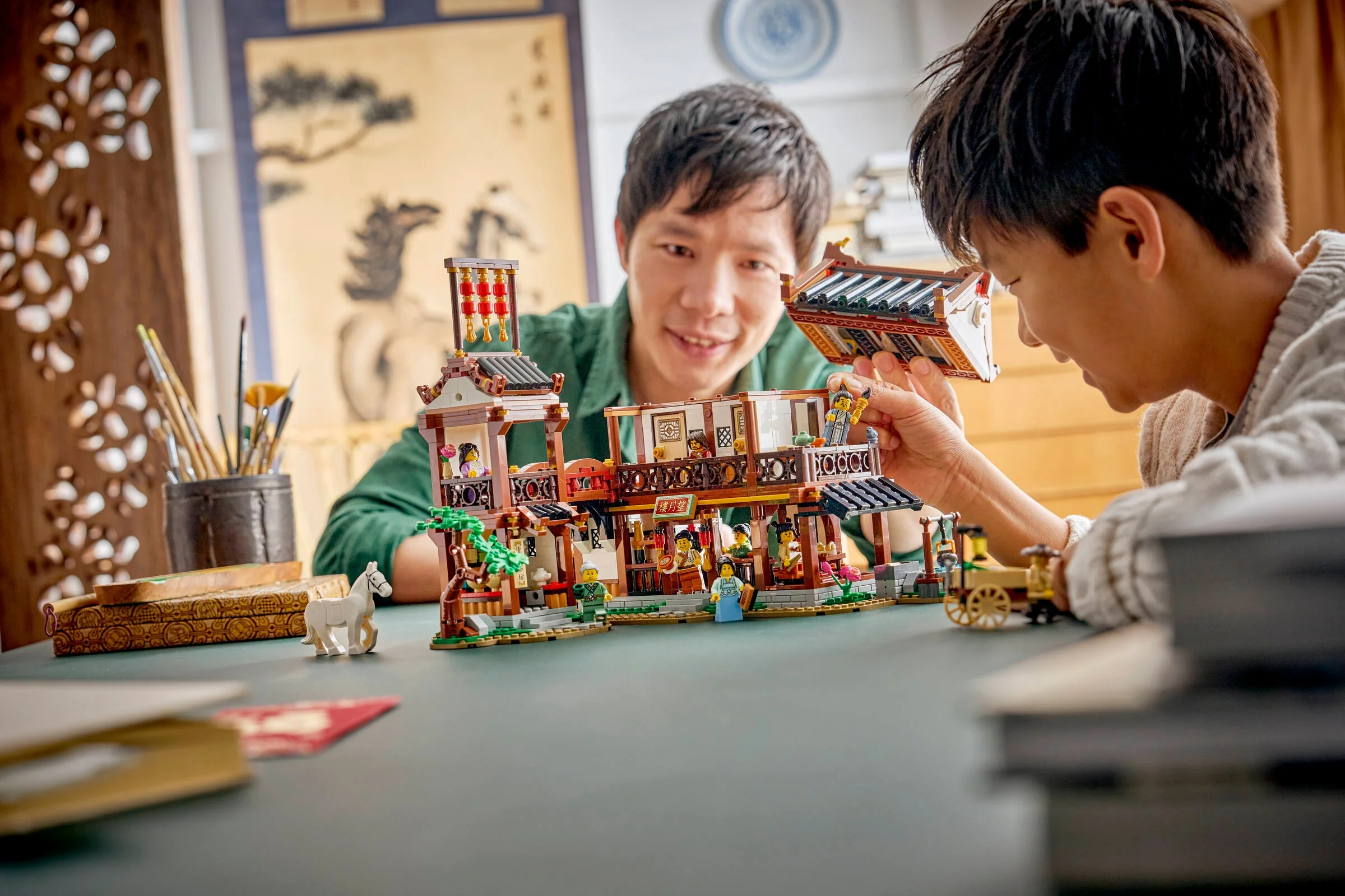 Un tată și fiul construiesc împreună hanul LEGO, bucurându-se de un moment special.