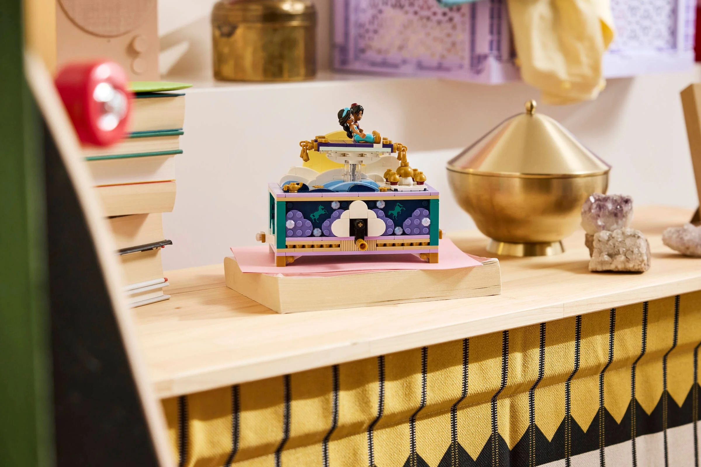 Cutie de bijuterii Jasmine LEGO pe o măsuță, decorată cu cărți și obiecte decorative.