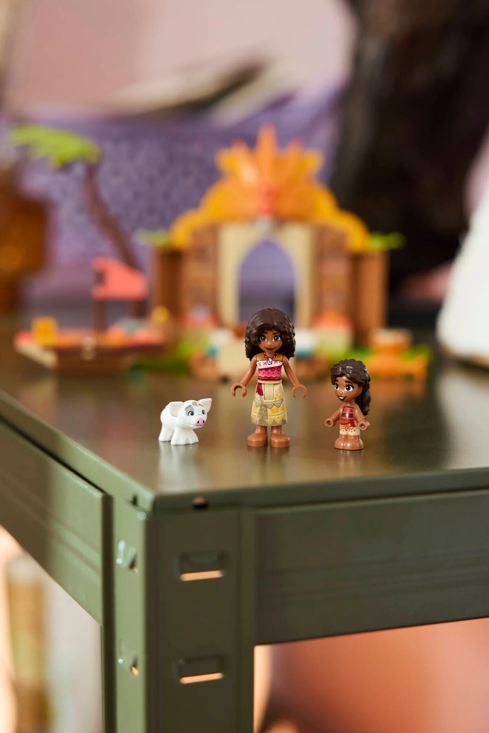 Mini-figurinele Moana și Pua stau pe o masă, cu casa și barca în fundal. Distracție la orizont!